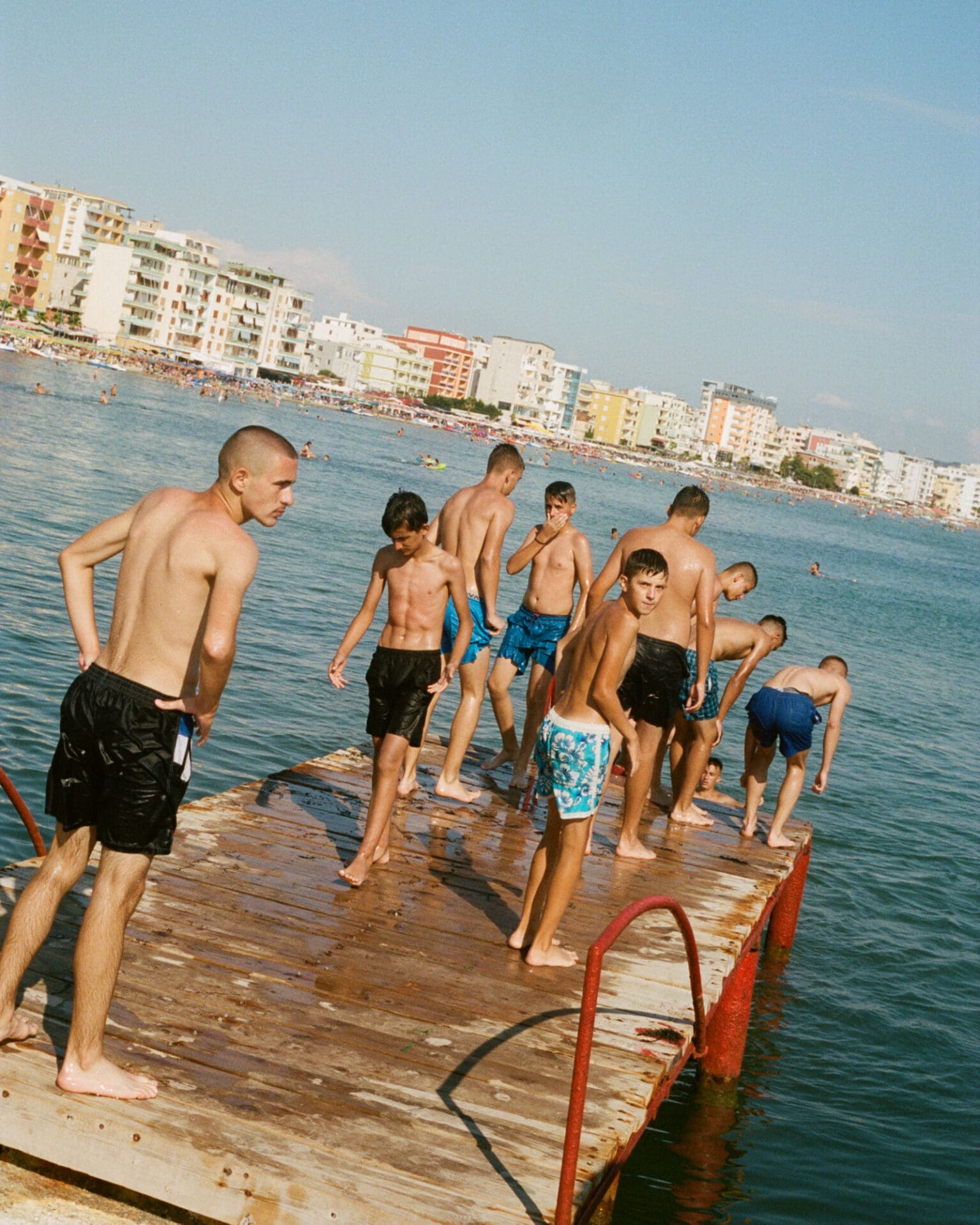 Hazel Gaskin photographs Albania | A group of boys on a wooden jetty jutting out into a body of water, getting ready to jump in