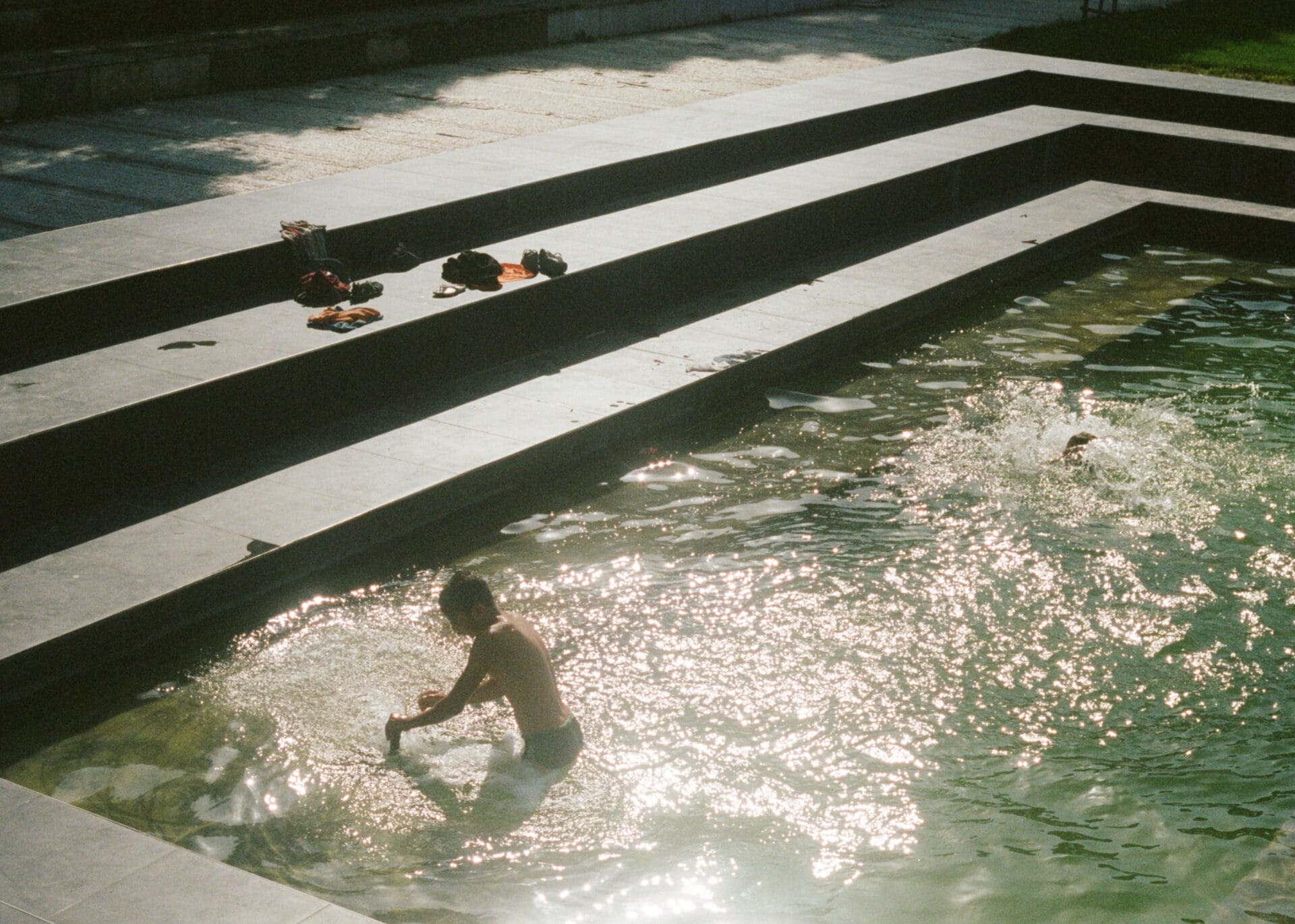 Hazel Gaskin photographs Albania | A boy plays in a rippling pool, with the sunlight flashing off the water's surface