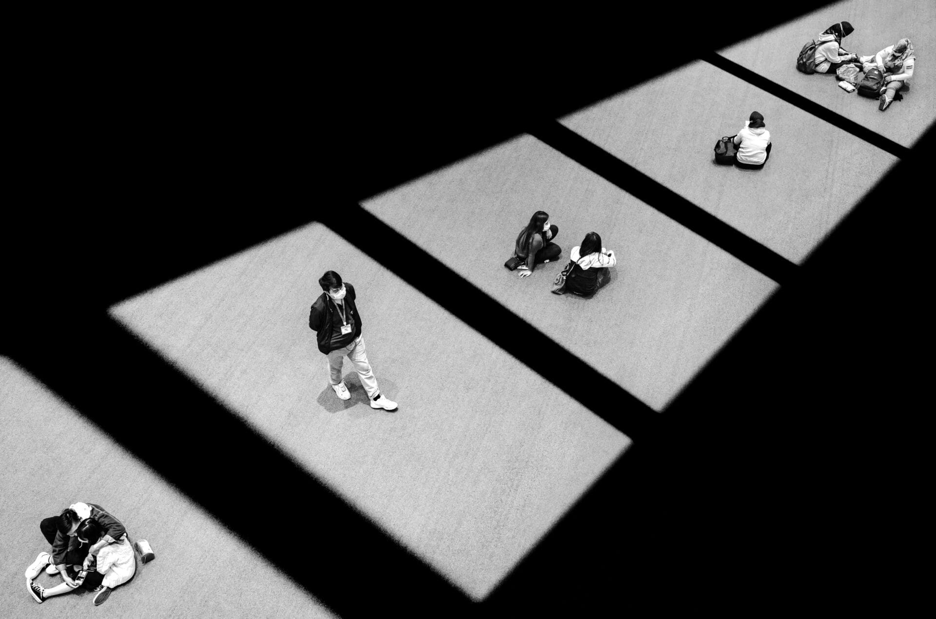 Jason Au | In Hong Kong's Tsuen Wan, groups of Hongkongers are sitting under a shopping mall atrium during the Covid-19 pandemic, sitting alone or in pairs. The walking man is an officer enforcing the 1.5m minimum social distancing rule.