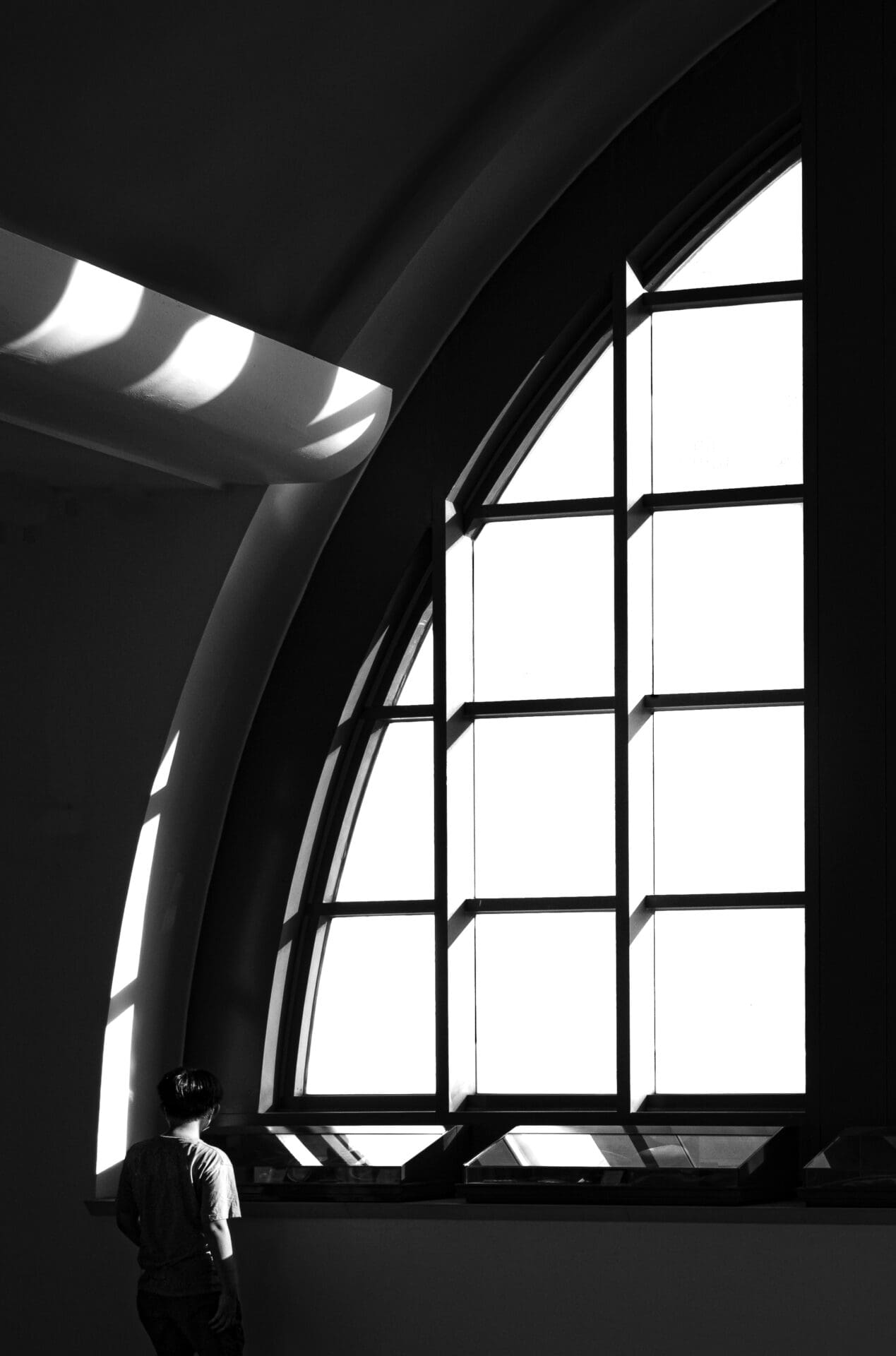 Jason Au | A man stands next to the window at Hong Kong ferry pier. His figure is side lit by a beam of late afternoon light.