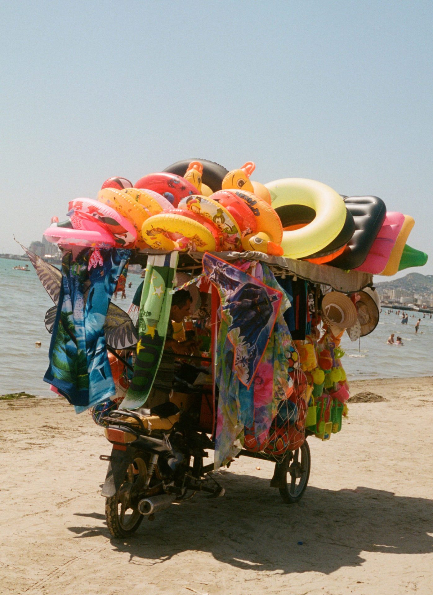 Hazel Gaskin | a cart on a beach in Durres groans with colourful merchandise, like inflatable rings in a rainbow of colours