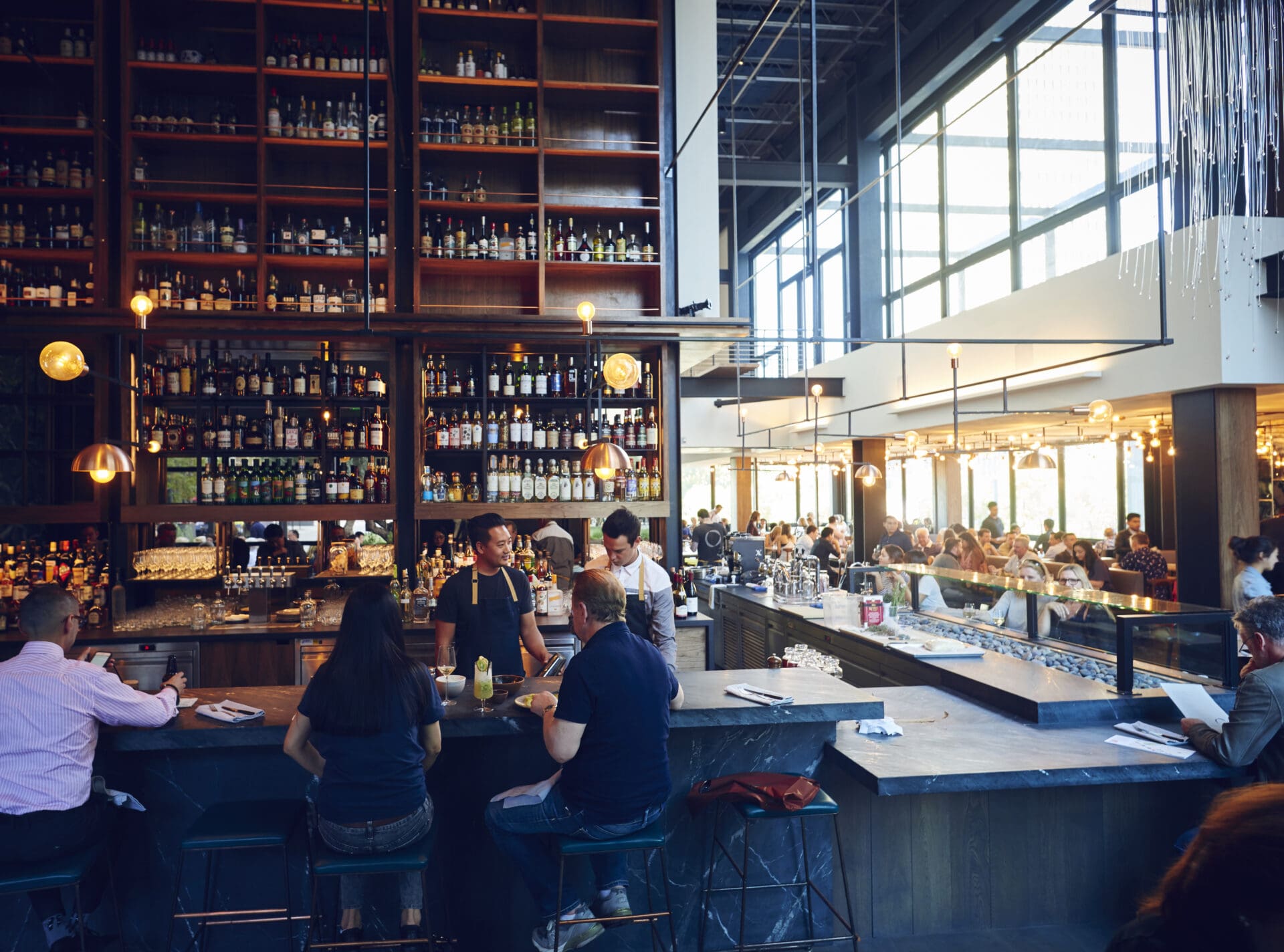 LA's best restaurants | A scene inside Otium, with people sat drinking at the bar, where tall shelves with bottles of spirits rise to the high ceiling