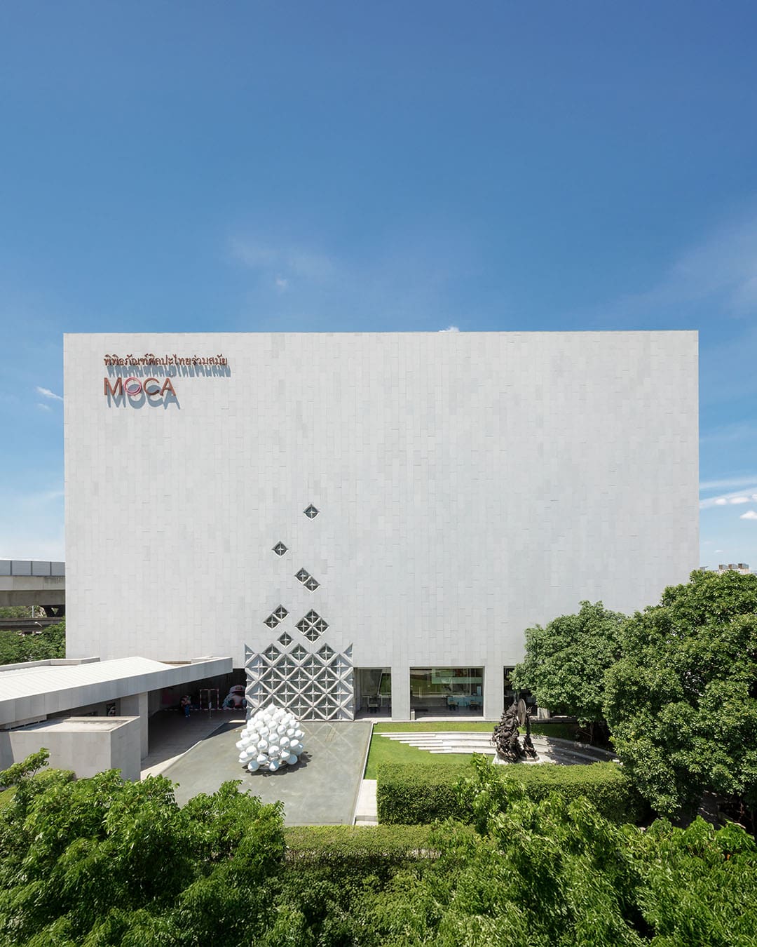 Modern exterior of MOCA Bangkok surrounded by trees and greenery