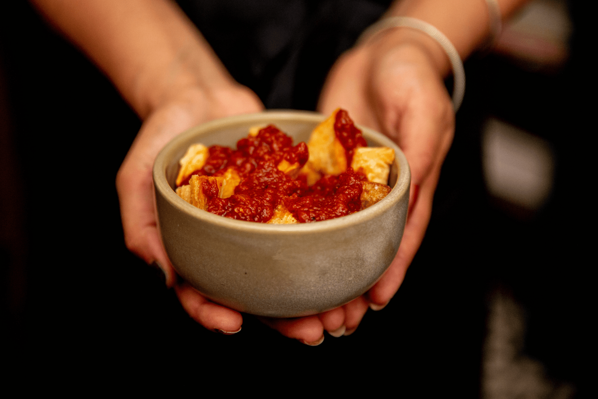 Tatale from Akwasi Brenya-Mensa | a pair of hands clasping a bowl of cassavas bravas, topped with a red tomato sauce