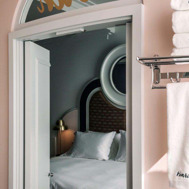 Where to stay in London | an arched doorway in a pink wall looking onto a bed with plush white sheets at Henrietta Hotel in Covent Garden