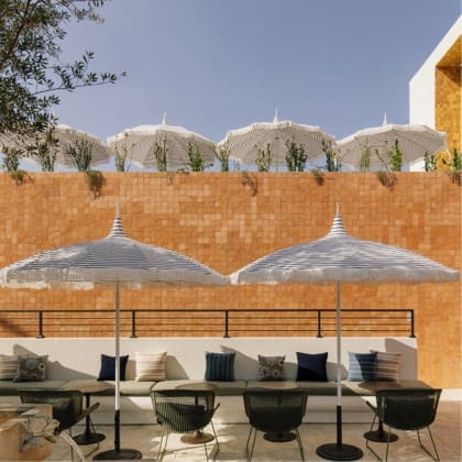 Pin-striped parasols framed by potted plants and an orange tiled wall at Silver Lake Pool & Inn