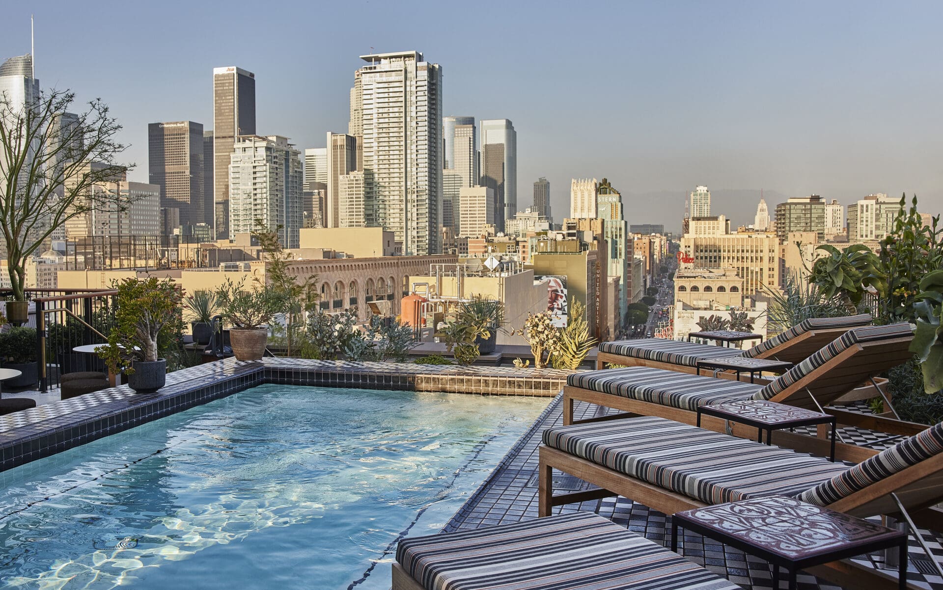 Best places to stay in LA | A rooftop scene at Downtown LA Proper, with a pool and deck chairs in the foreground, and a cityscape of downtown LA in the background
