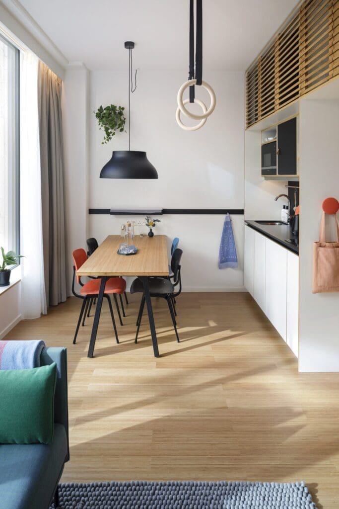 Hotels and digital nomads | The living space at Zoku Loft, Amsterdam, with a blue sofa, a kitchenette and exercise hoops in a white-walled room with a light-wood floor