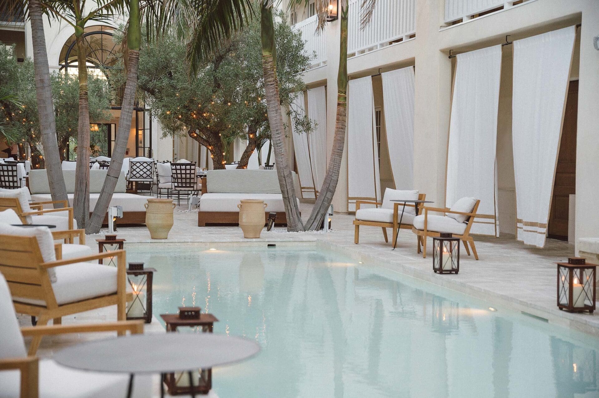 Best places to stay in LA | A scene of the central courtyard at Cara, with a pool, armchairs, lanterns, and hanging linen drapes.