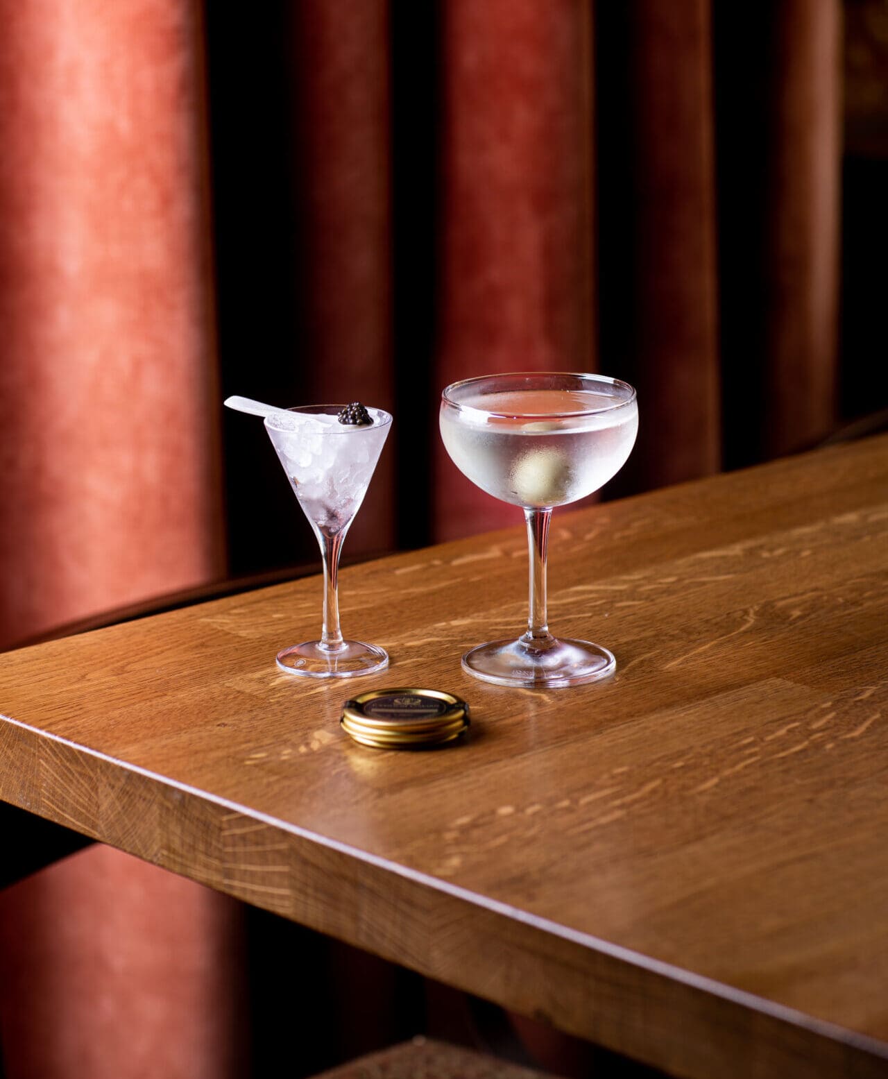 London's best bars | Two ice-cold cocktails in a coupe and a martini glass on a wooden table with a red backdrop at The Cadogan Arms
