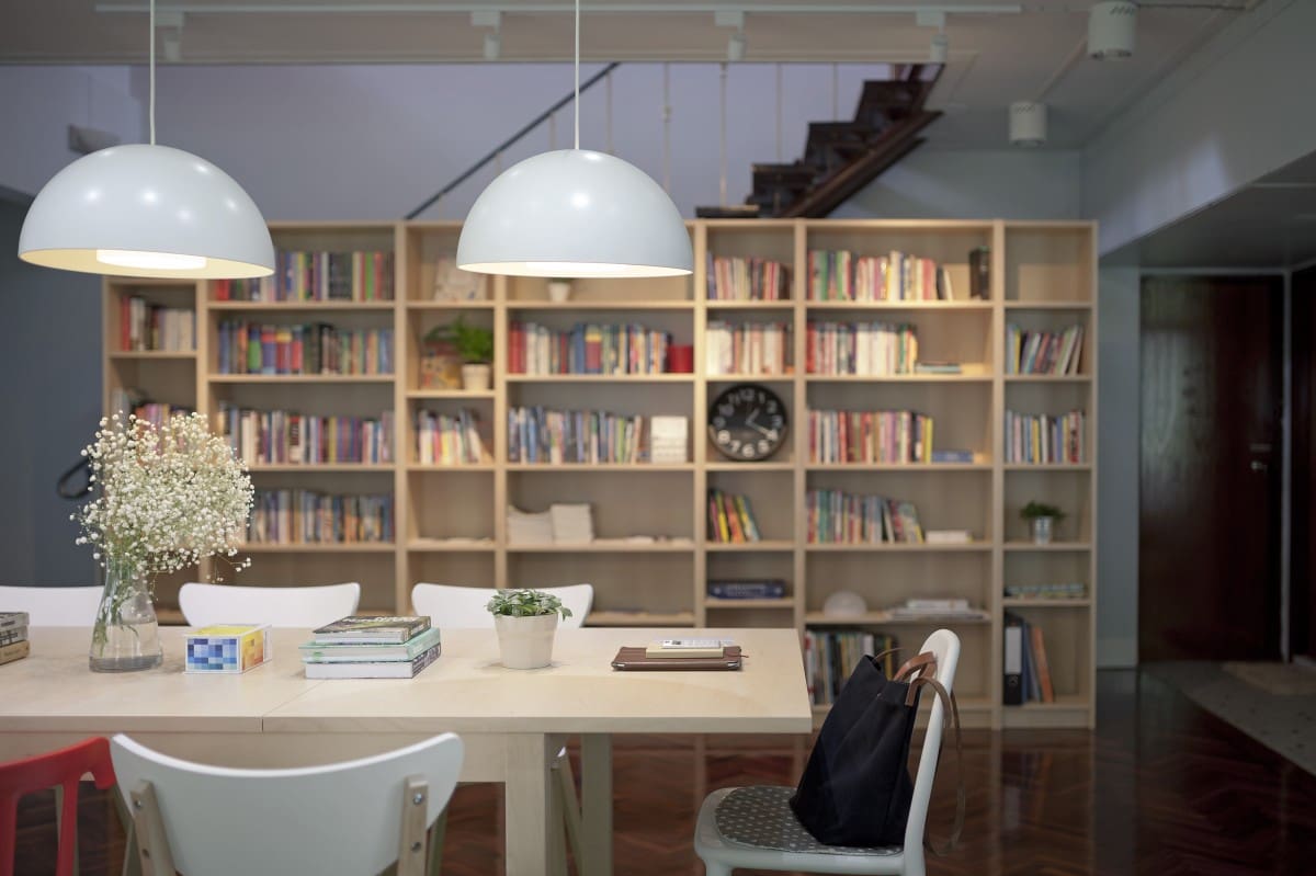 Where to co-work in Bangkok | A library style space with communal working desk, bookshelves and a semi-circular overhead light at Muchroom