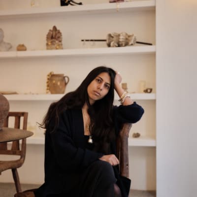 Rosh Mahtani, Alighieri | the designer wearing head-to-toe black in front of some shelves in her studio