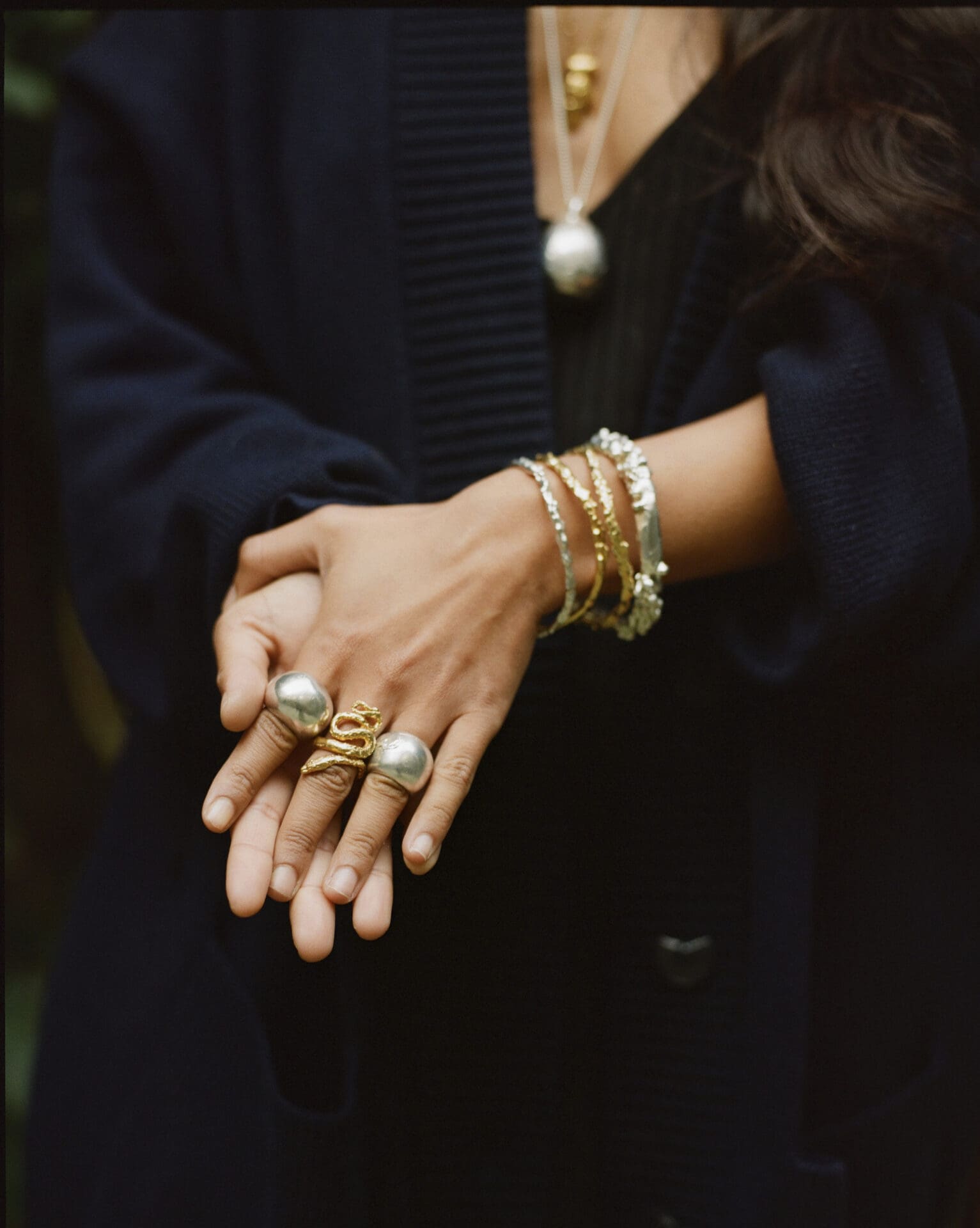 Rosh Mahtani, Alighieri | Rosh wearing a black top, clasping her hands with lots of Alighieri jewellery