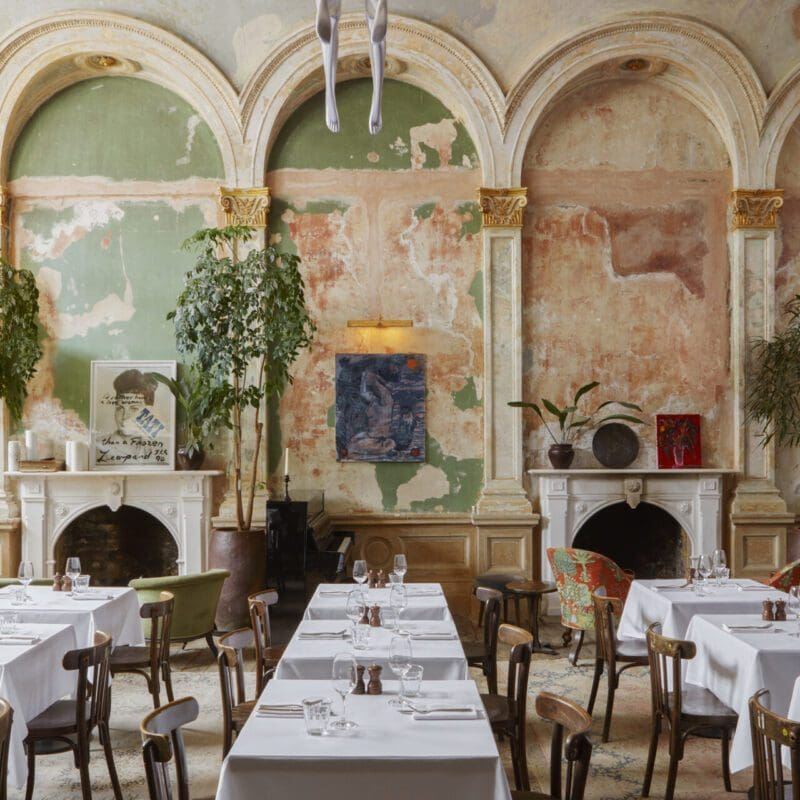Best restaurants in London | Tables lie in wait with cutlery and pristine white tablecloths in the dining room at Sessions Arts Club, in front of bare stripped walls and twin fireplaces