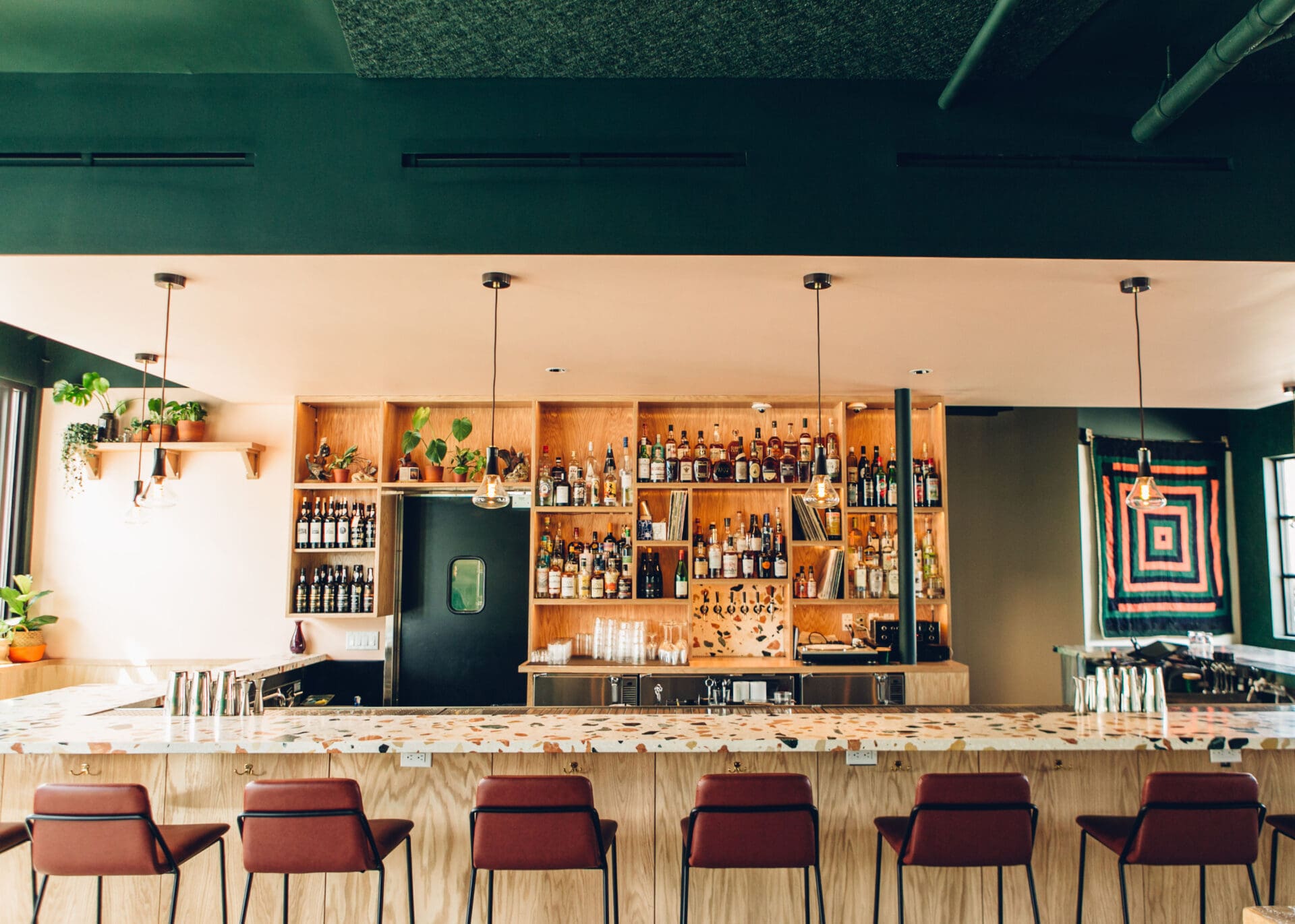 Los Angeles best cocktail bars | A view of the bar at Thunderbolt, where high red chairs line a terrazzo bar top, and drinks line the shelves. A green ceiling can be seen
