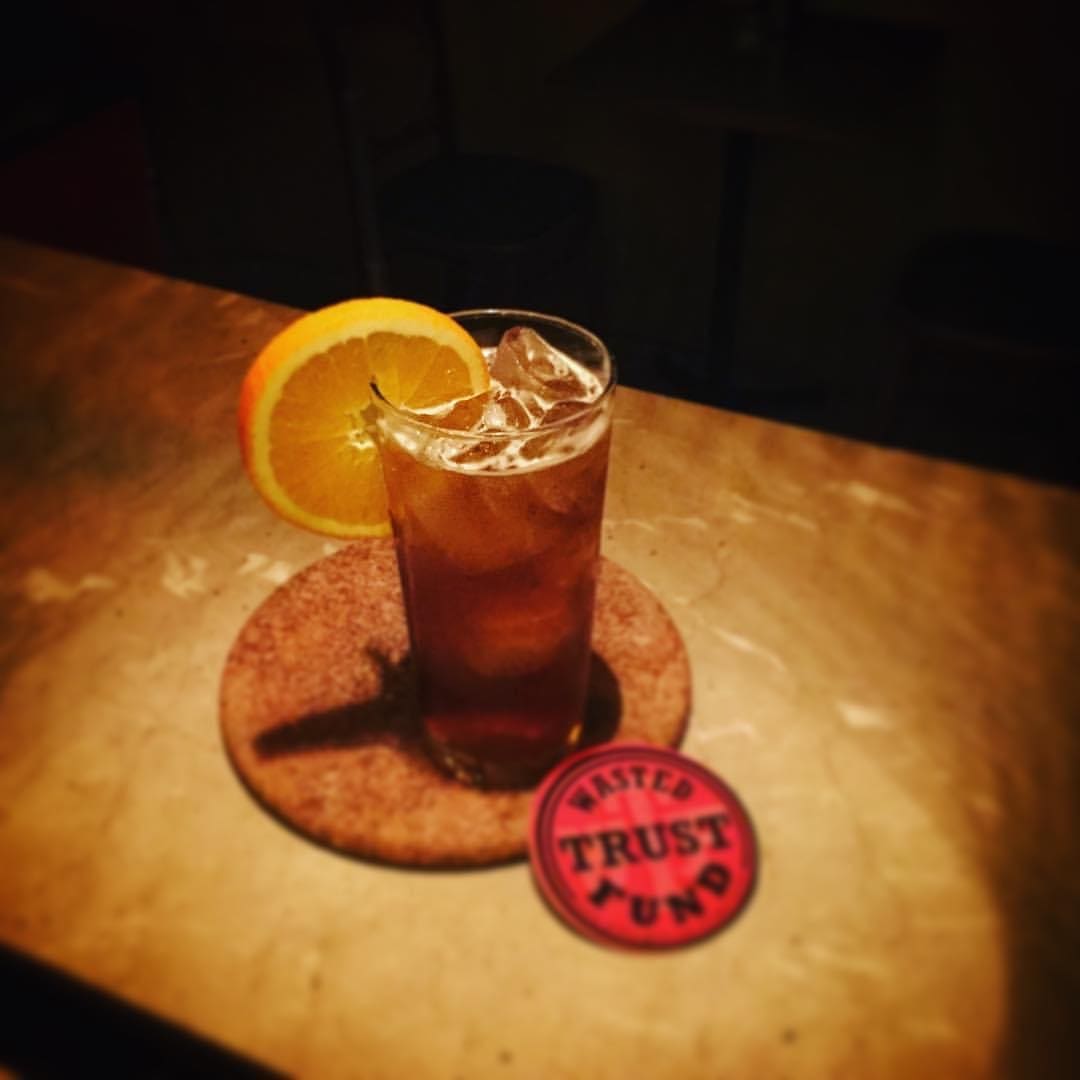 Best Bangkok bars | A drink garnished with an orange wheel in a tall glass on a coaster that reads 'Wasted Trust Fund' at WTF