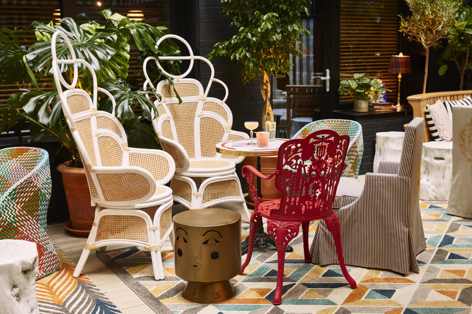 A view of the courtyard at Mama Shelter in Shoreditch, London. A mismatched assortment of chairs are arranged around a table, and multi coloured tiles decorate the floor.