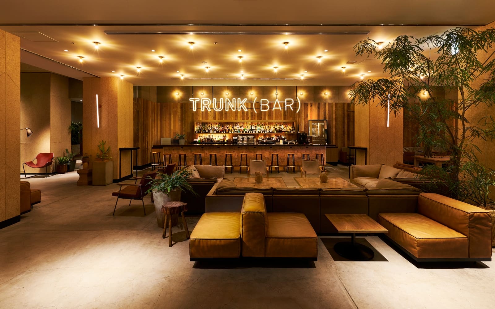 Hotels and digital nomads | The communal bar area at Shibuya Trunk hotel Tokyo, with low wooden furniture, mustard-yellow leather sofas and oriental-inspired greenery, in front of the long bar