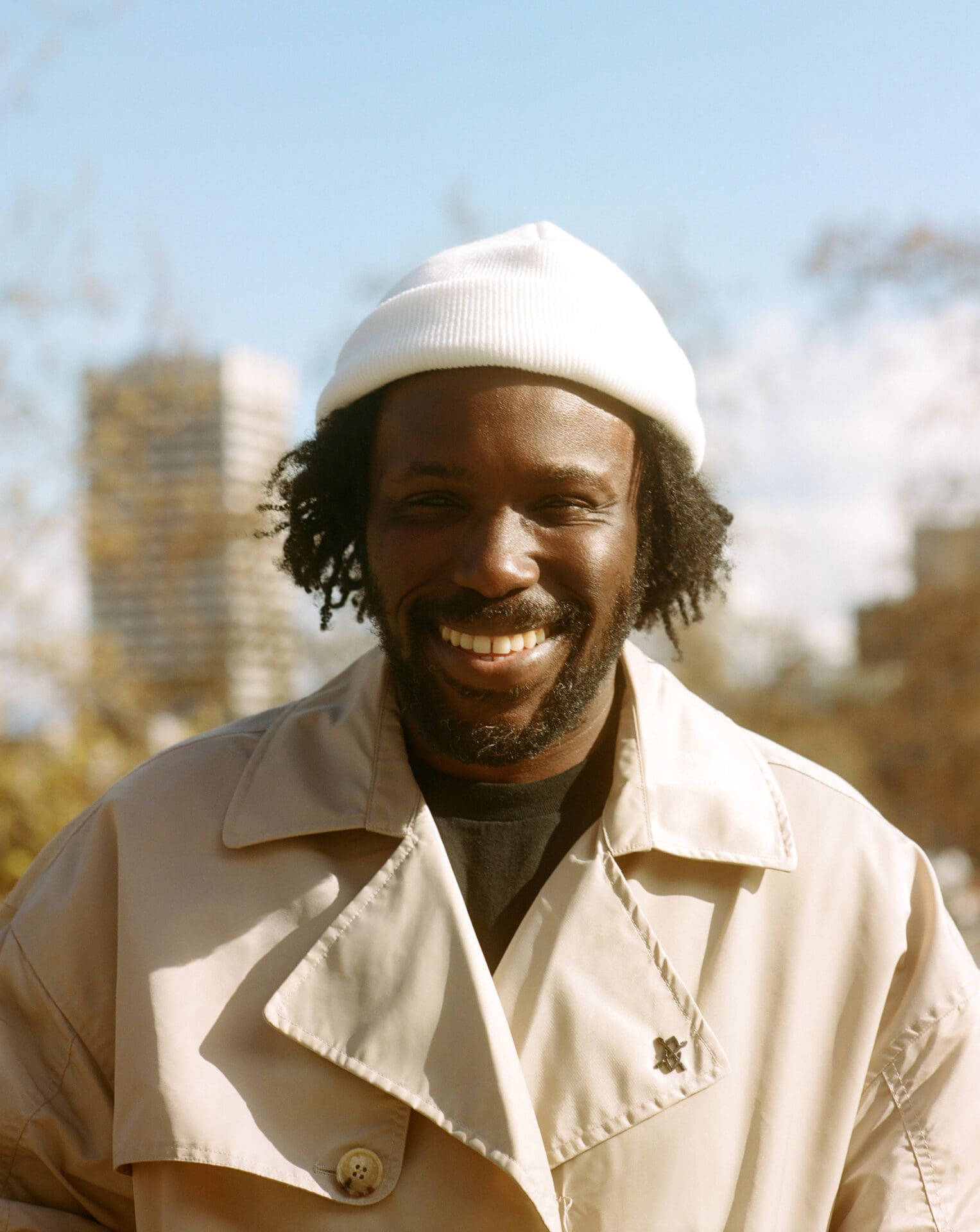 Akwasi Brenya-Mensa | The chef wearing a white beanie and beige trench coat smiling into the sun