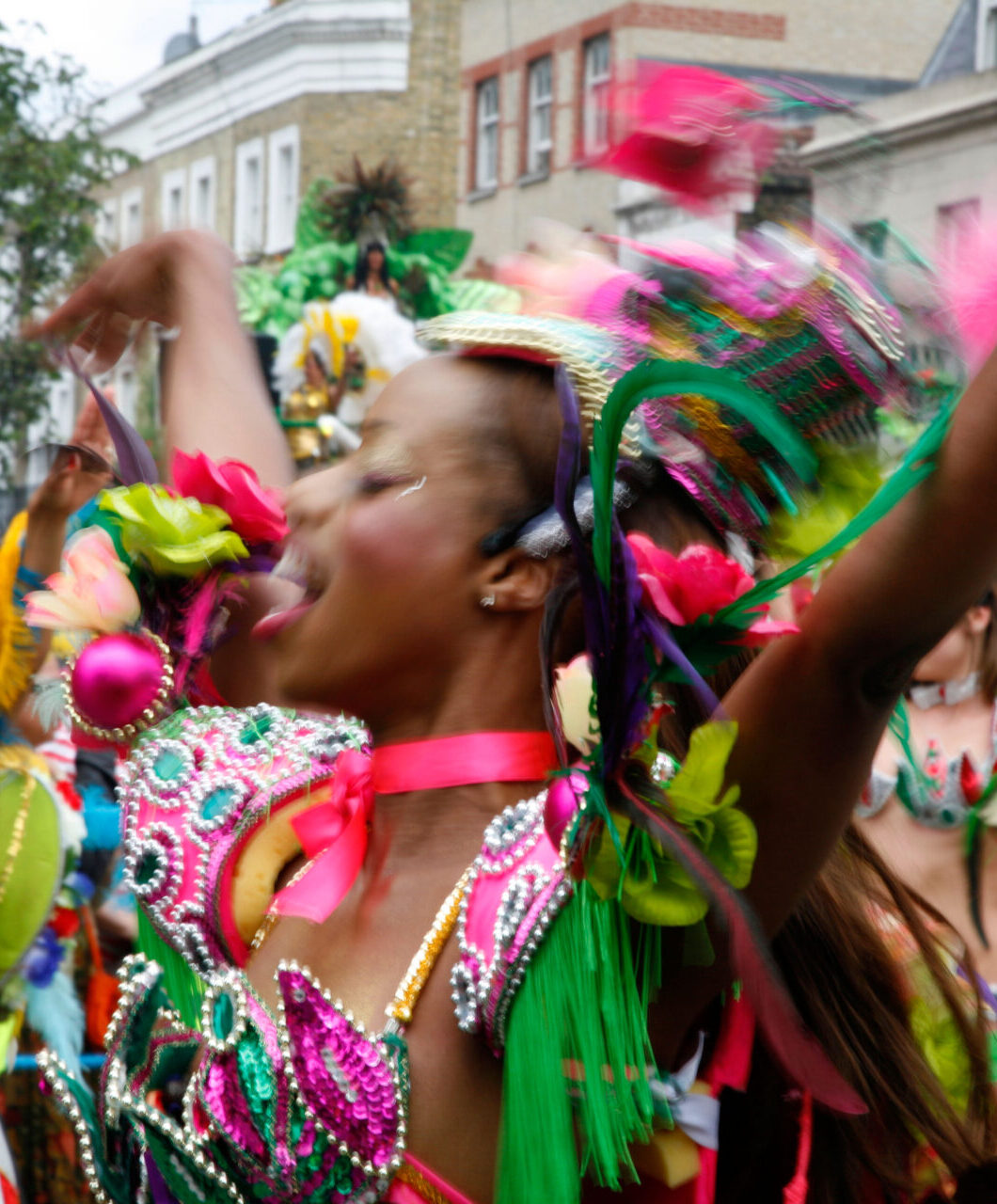 London's Caribbean community | A woman wearing a vibrant pink-and-green costume dancing in a parade at London's Notting Hill Carnival