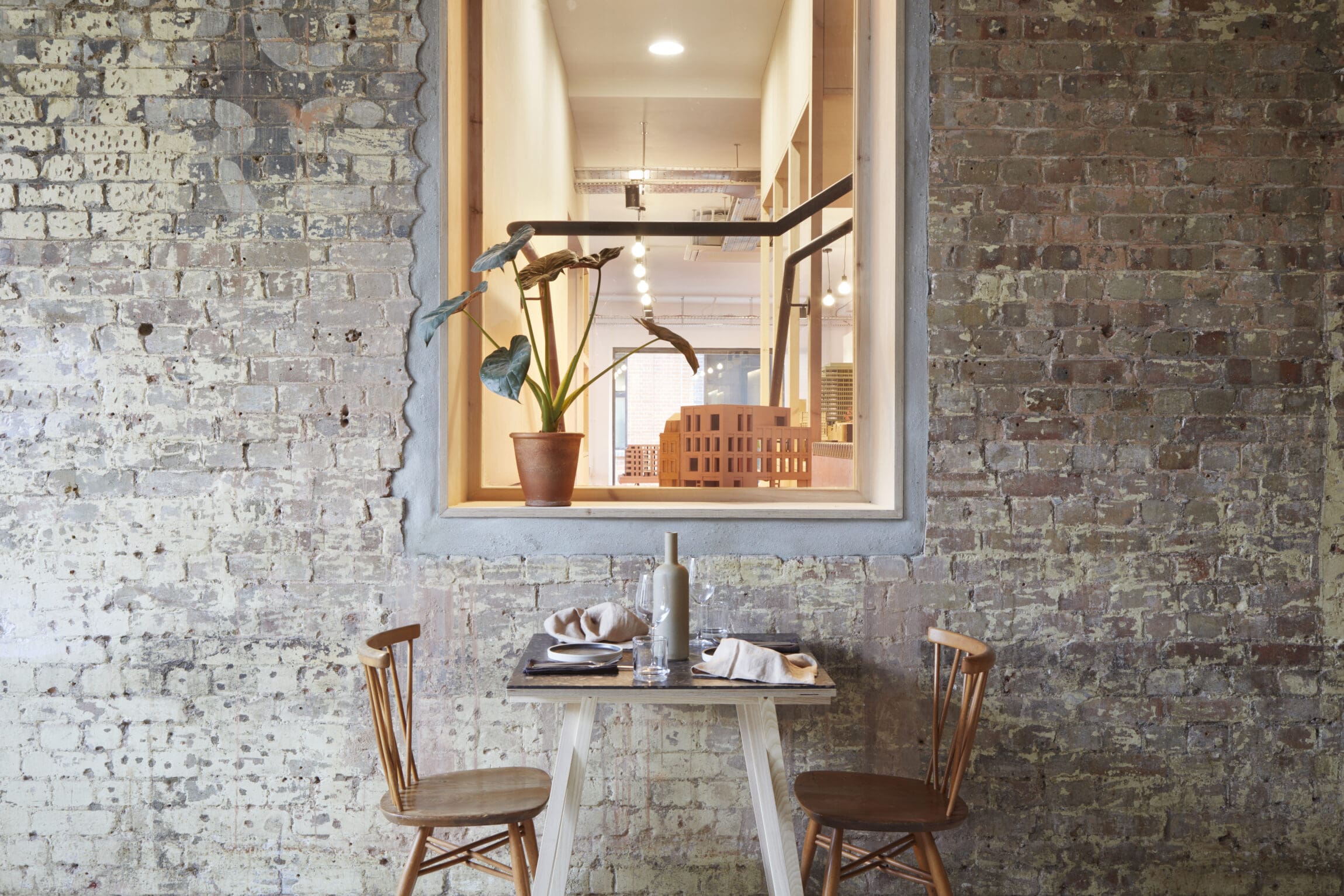 The best restaurants in Hackney | A table and two chairs stand before an exposed brick wall with a window frame opening above it where a pot plant sits.