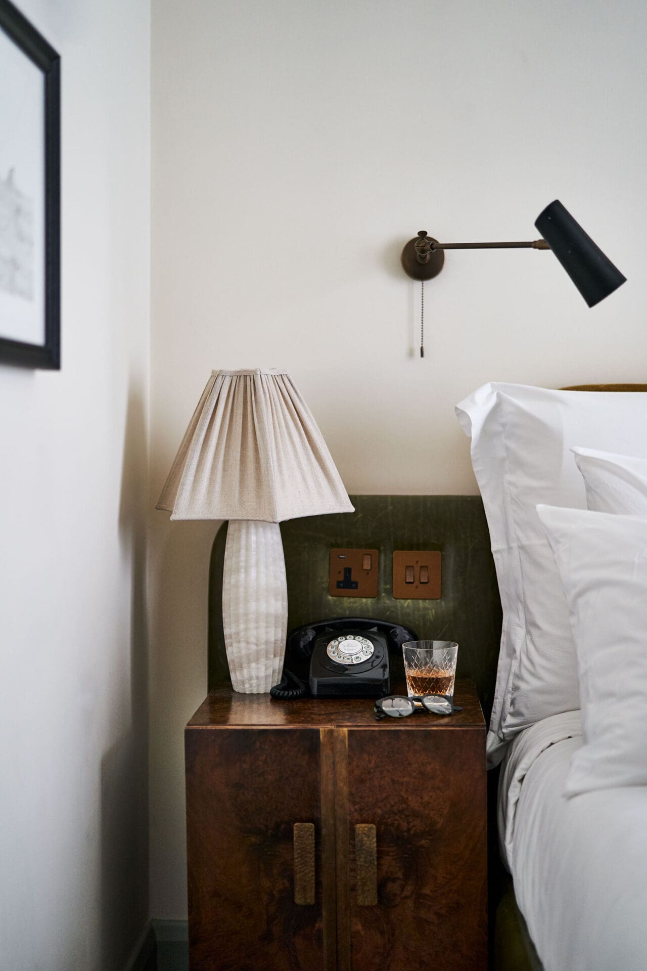 Best hotels in Shoreditch, Dalston and Hackney | A bedside table with a drink and sunglasses on it, beside a bed in one of the rooms at Redchurch Townhouse