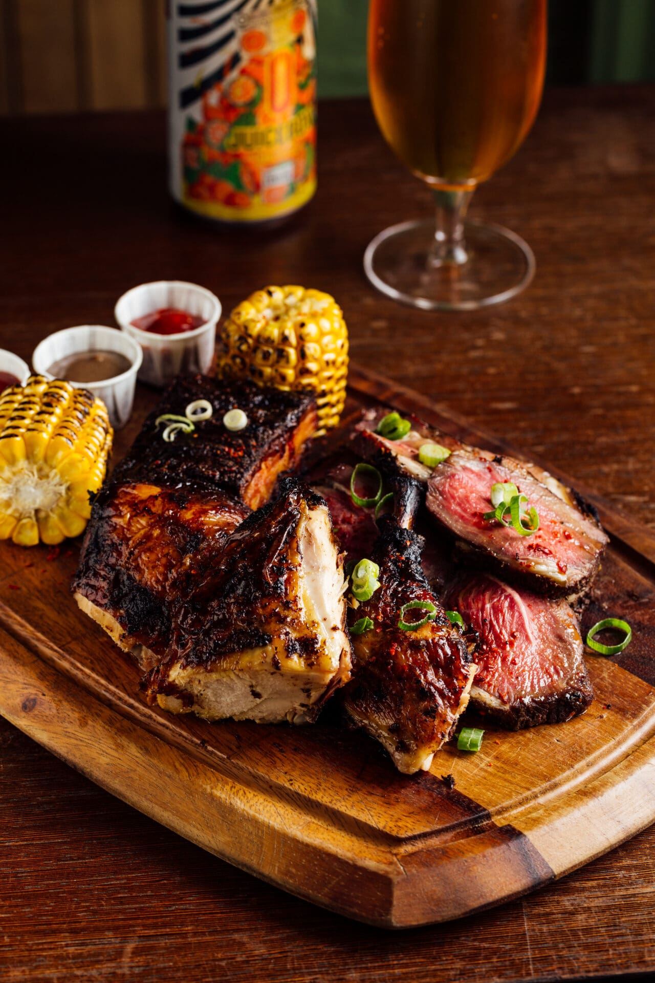 London's Caribbean community | Jerk-marinaded meat served on a wooden board with corn on the cob and a can and a cold glass of beer in the background