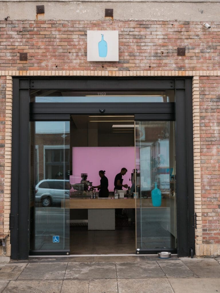 LA's best coffee shops | The exterior of the Blue Bottle's Abbot Kinney coffee shop, with bare brick walls, glass doors and the blue bottle logo above the door
