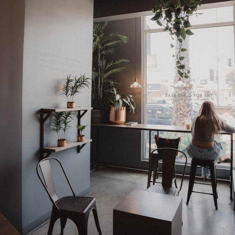 LA's best coffee shops | A girls sits on the stool in the window of The Boy and the Bear, looking out onto the street. Grey walls, grey metal furniture and plenty of greenery give an industrial-chic vibe.