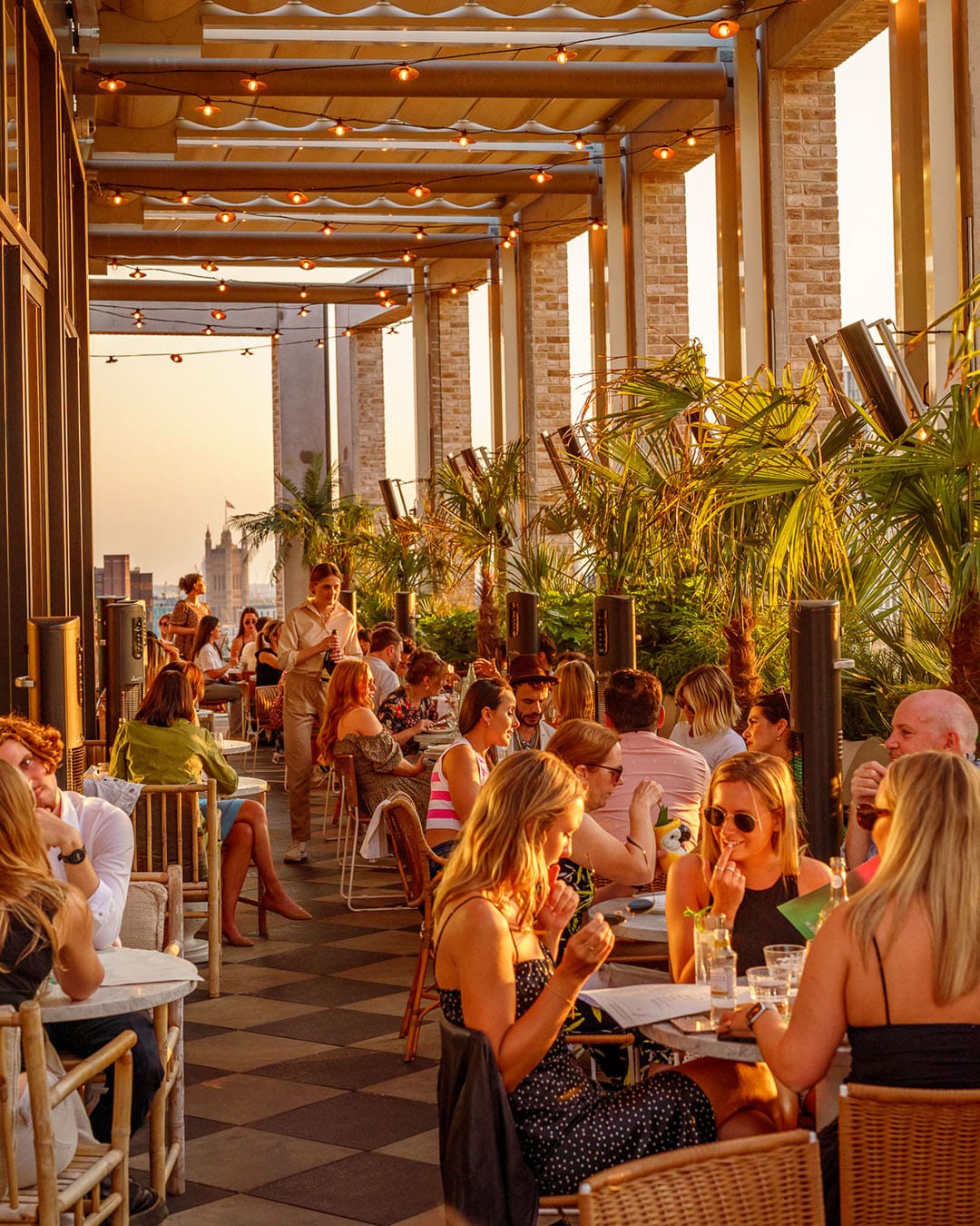 People at rooftop bar enjoying drinks, food and good conpany in the summer sun at Seabird, The Hoxton Southwark