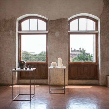 Best art galleries in Mumbai | A view of an installation of sculptures by Rana Begum inside Jhaveri Contemporary gallery in Mumbai. Outside, through two arched windows, you can see a green view of Mumbai, with a fort in the background.