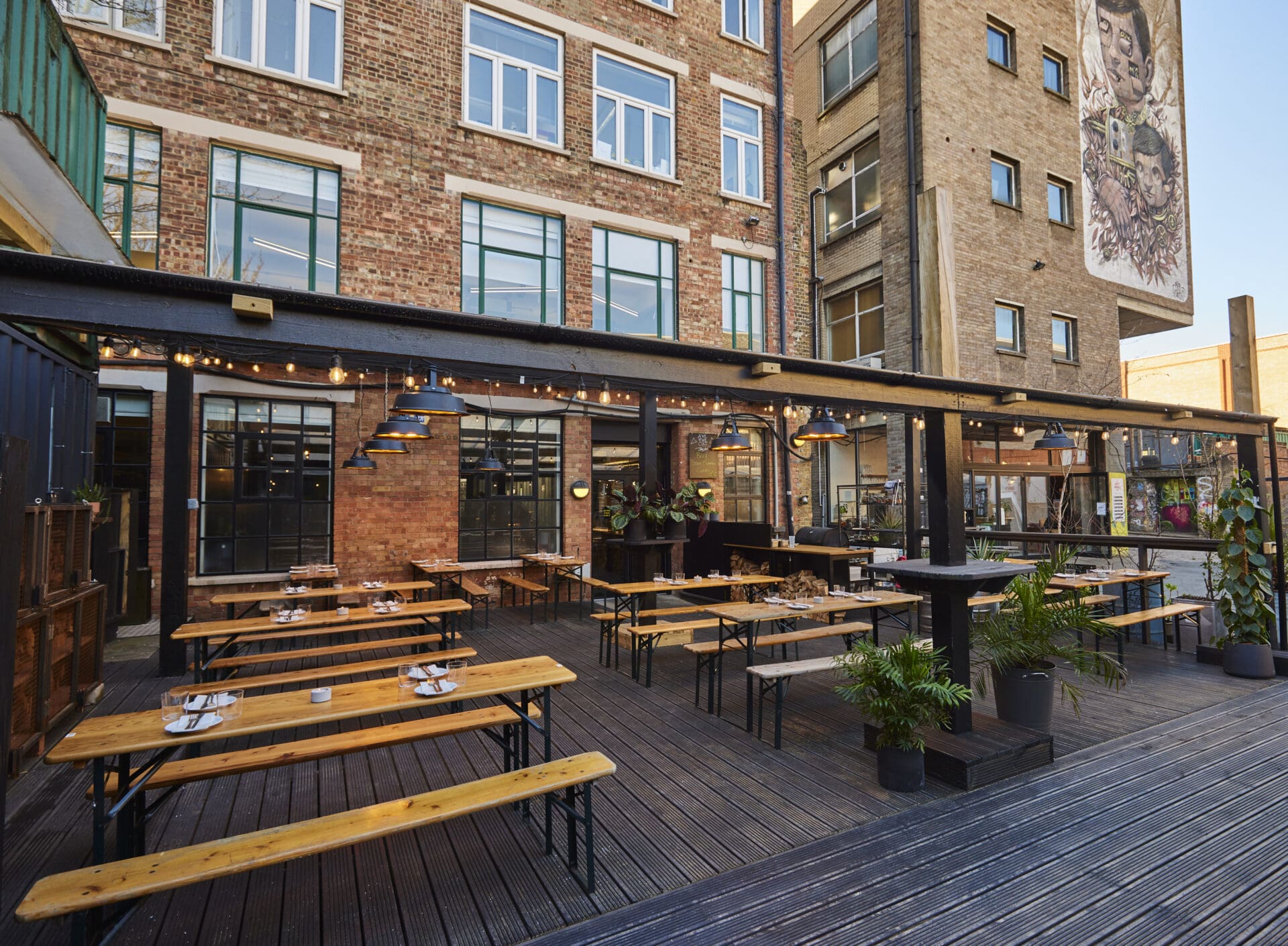 Best restaurants with outdoor seating in London | Grey wooden floors and brown-wood tables and benches outside Acme Fire Cult in Dalston