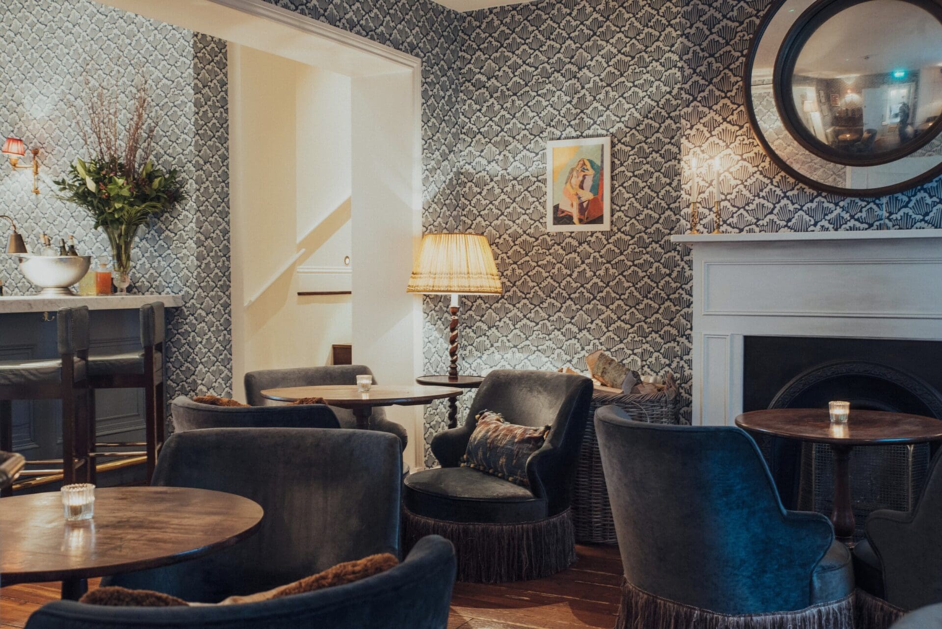 Isle of Wight | Blue painted wallpaper provides a backdrop to blue velvet armchairs, dark-wood tables and old-fashioned English furnishings, including a white fireplace, at North House