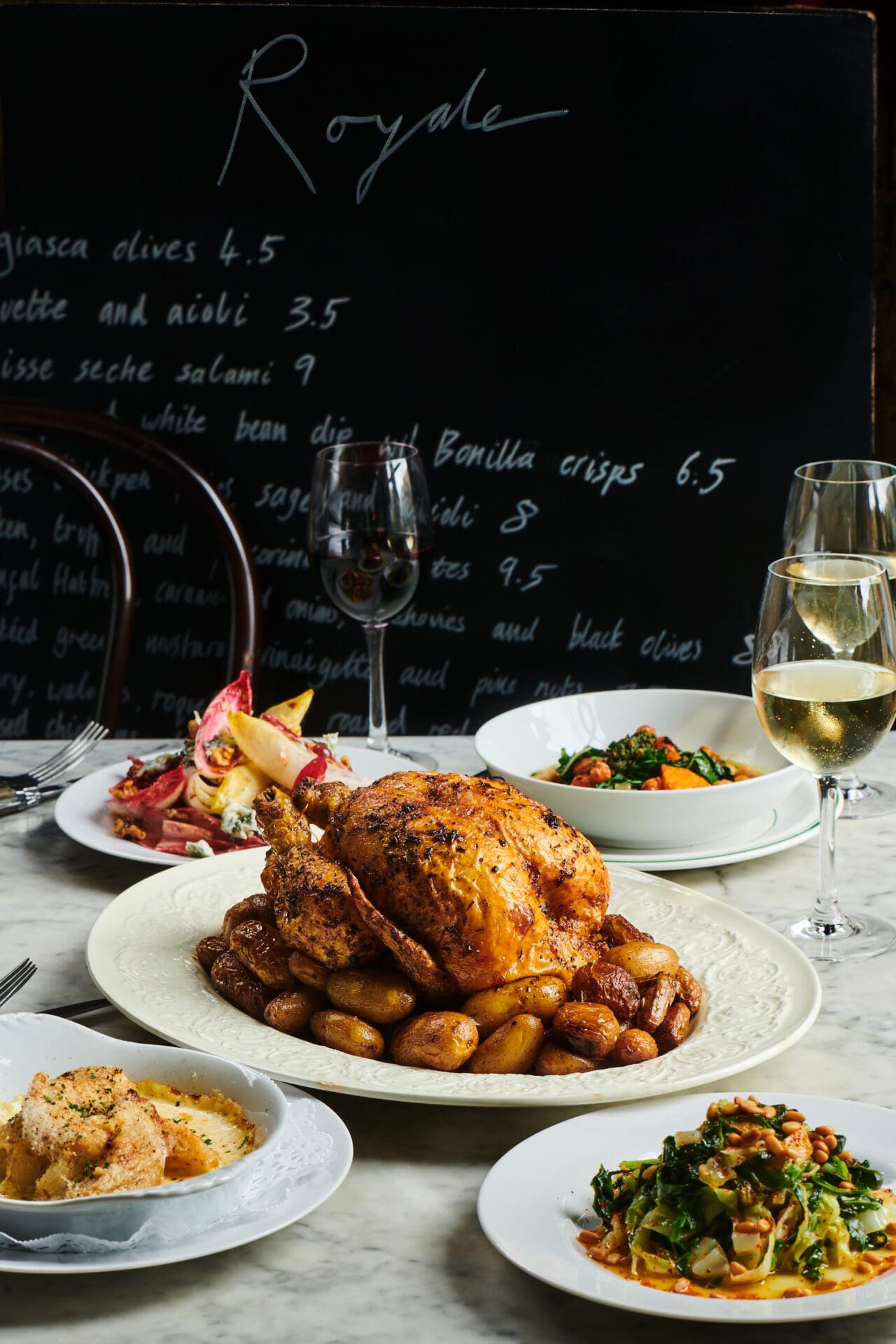 Best restaurants with outdoor seating in London | a roast chicken on a bed of new potatoes, on a white oval plate, in front of several other dishes