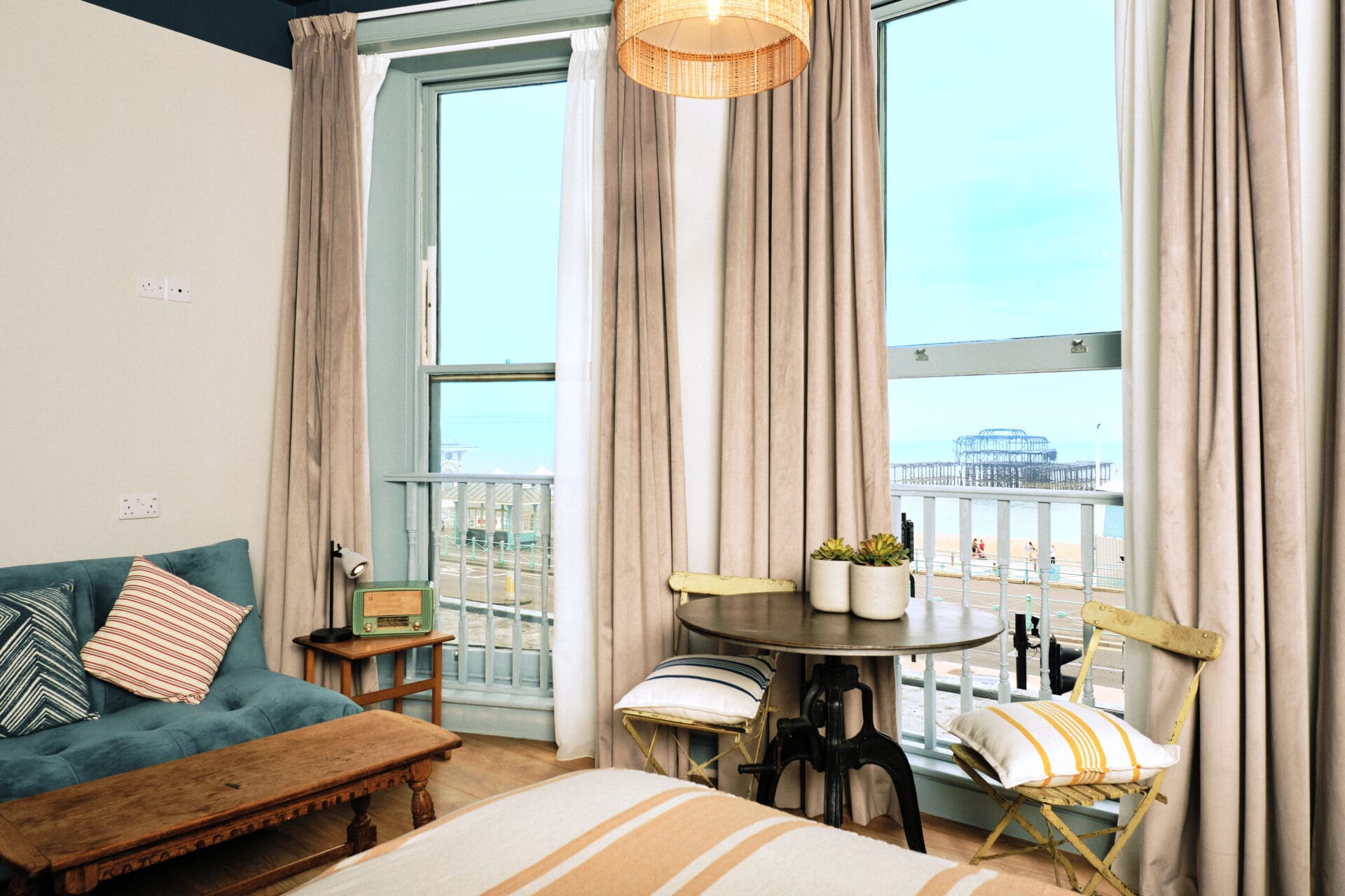 The Selina hotel in Brighton | a velvet sofa beside two floor to ceiling windows overlooking Brighton beach