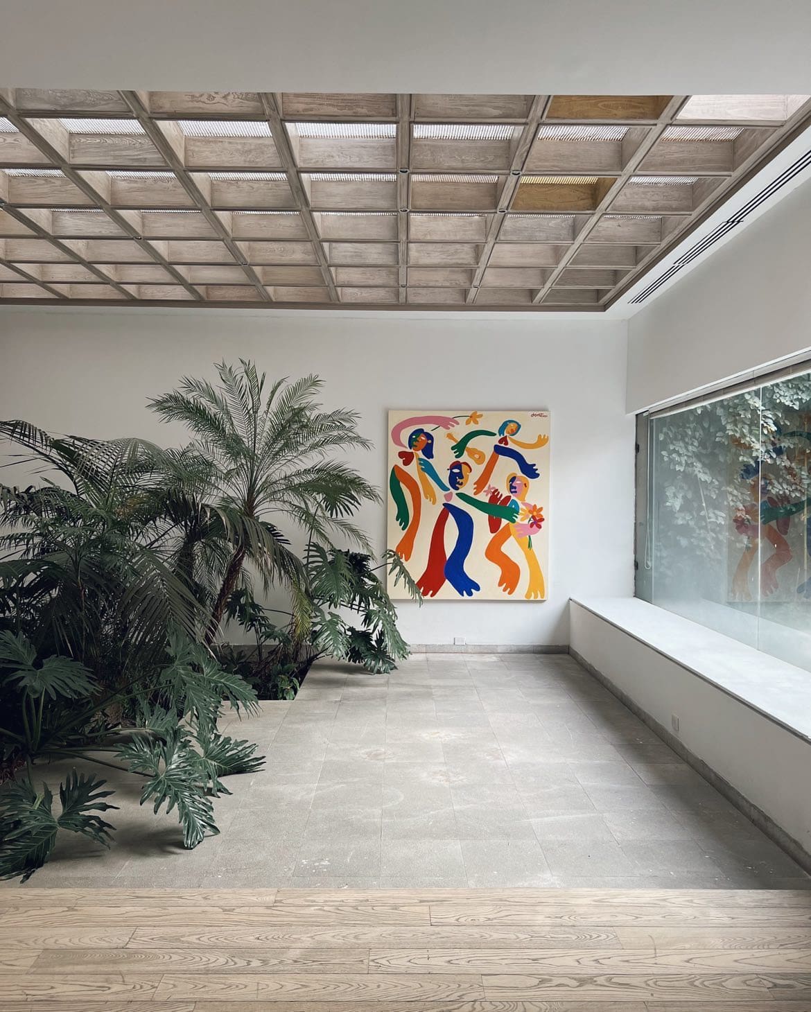 The best art galleries and museums in Mexico City | Inside JO-HS gallery, where leafy plants contrast with a concrete floor and white walls, and a painted work of art is on display on a wall.