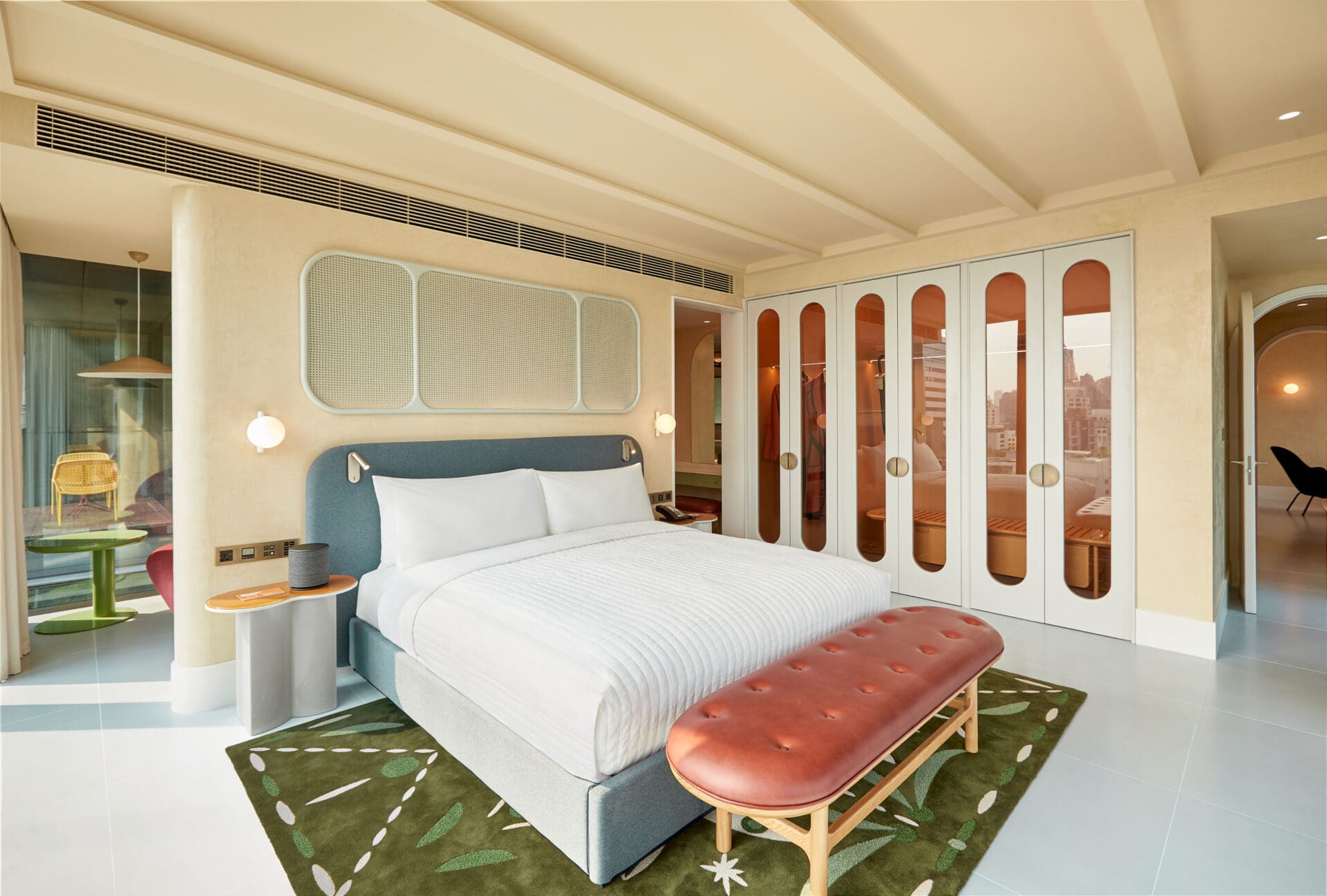 The Standard Bangkok Mahanakhon hotel opening | A bed with white sheets on a blue-grey cushioned frame, on a green patterned rug