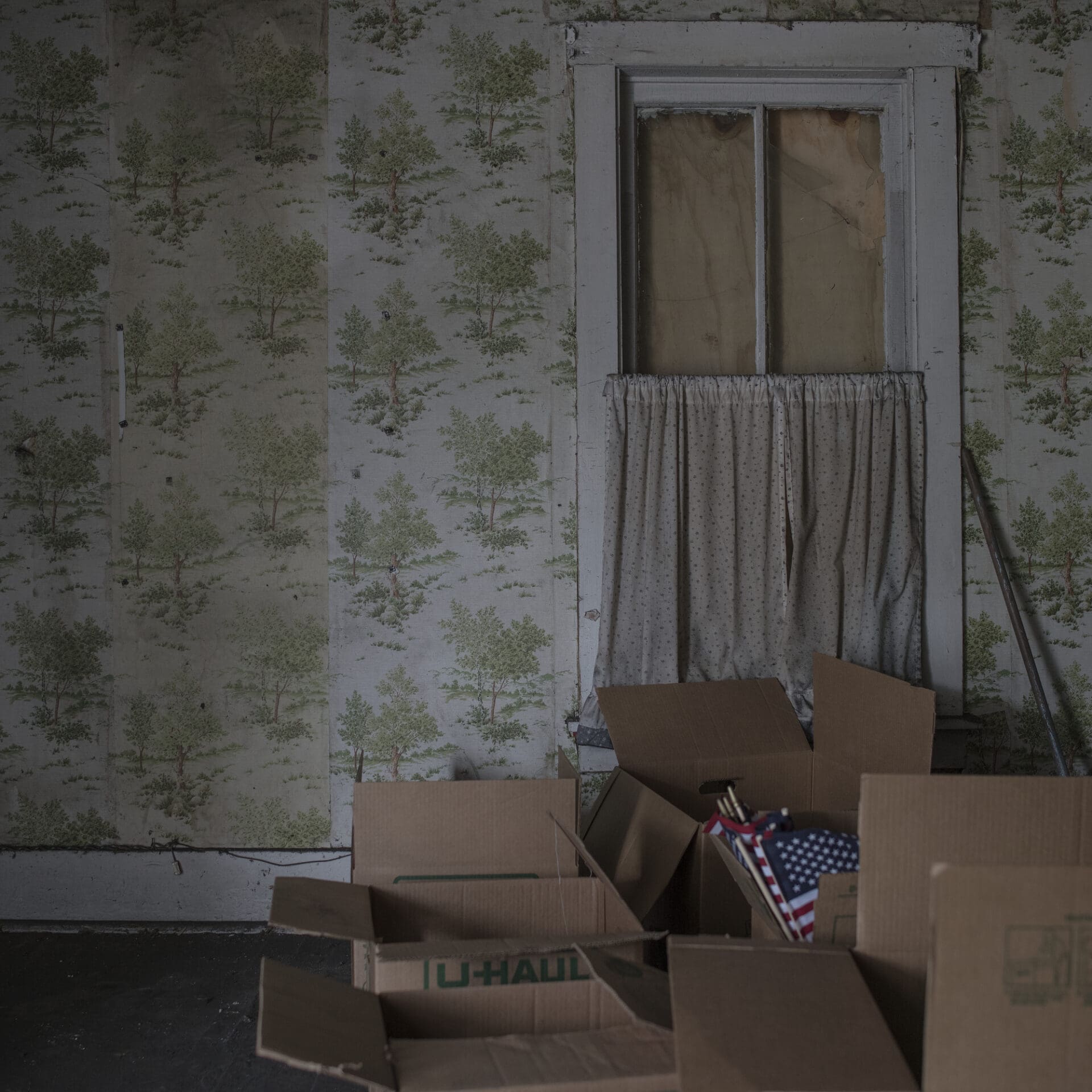 Photographer Rich-Joseph Facun | empty battered cardboard boxes sit in front of peeling, patterned green wallpaper and a boarded up sash window