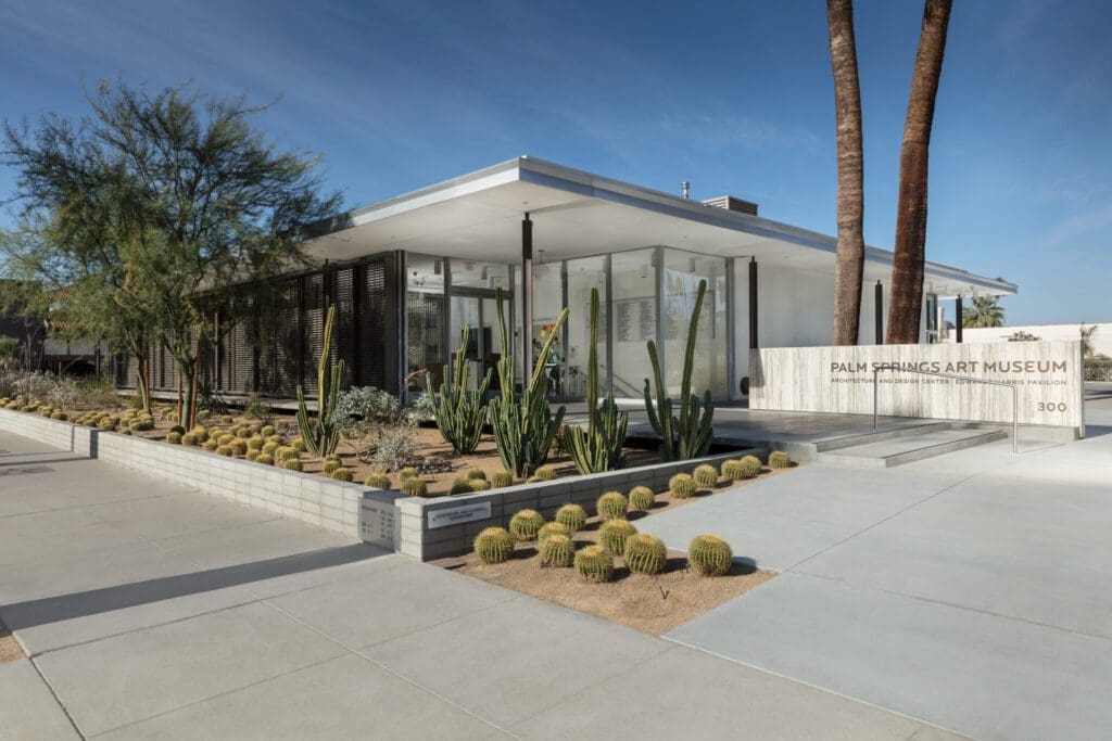 What to do in Palm Springs, California | The exterior of Palm Springs Art Museum, a low, flat-ceiling building with glass walls and surrounded by desert vegetation