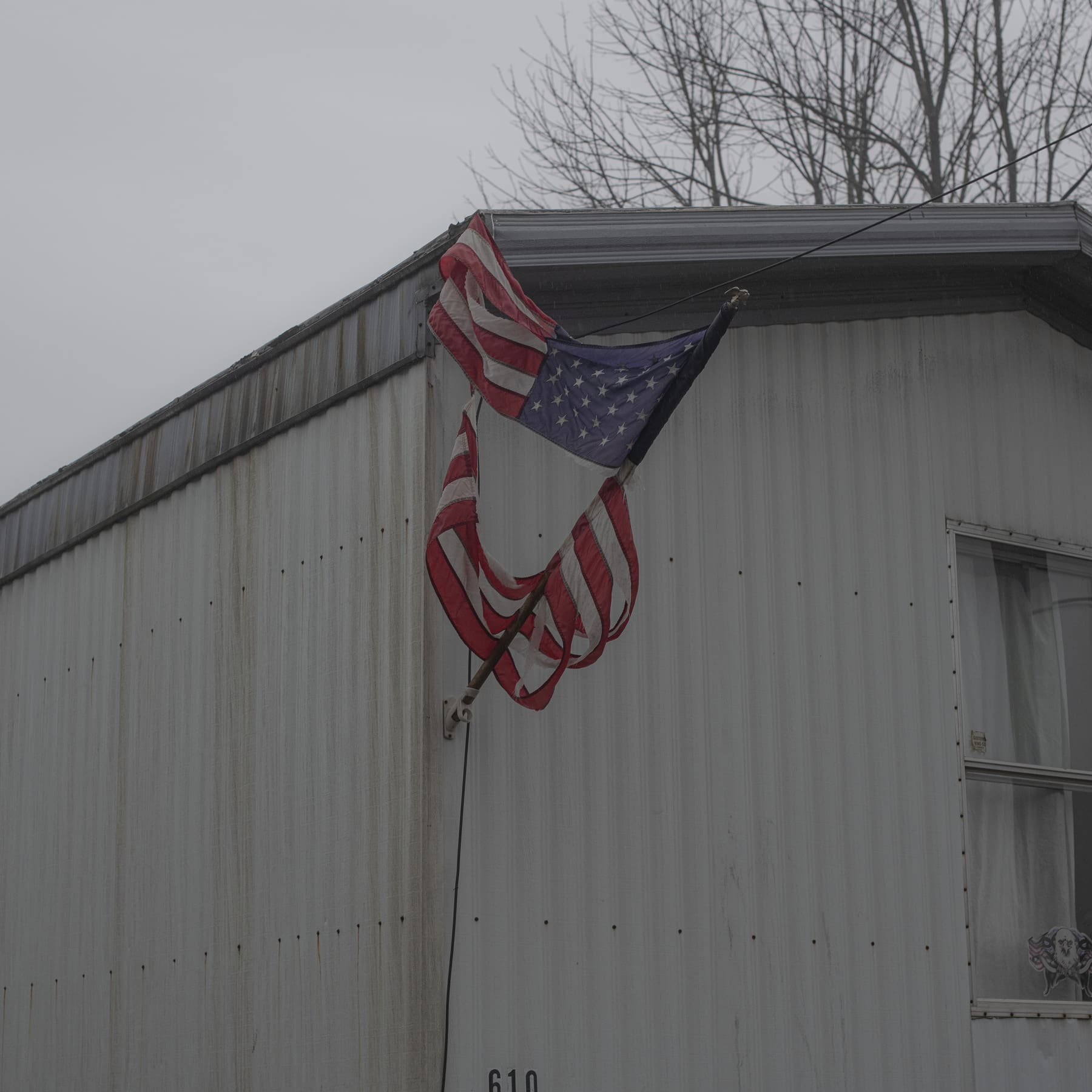Photographer Rich-Joseph Facun | A battered American flag blows against a white-board building, against a pale-grey sky