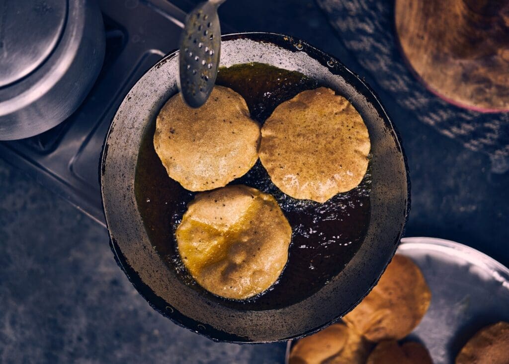 The best street food in Mumbai | A small saucepan with three puri deep frying in oil.