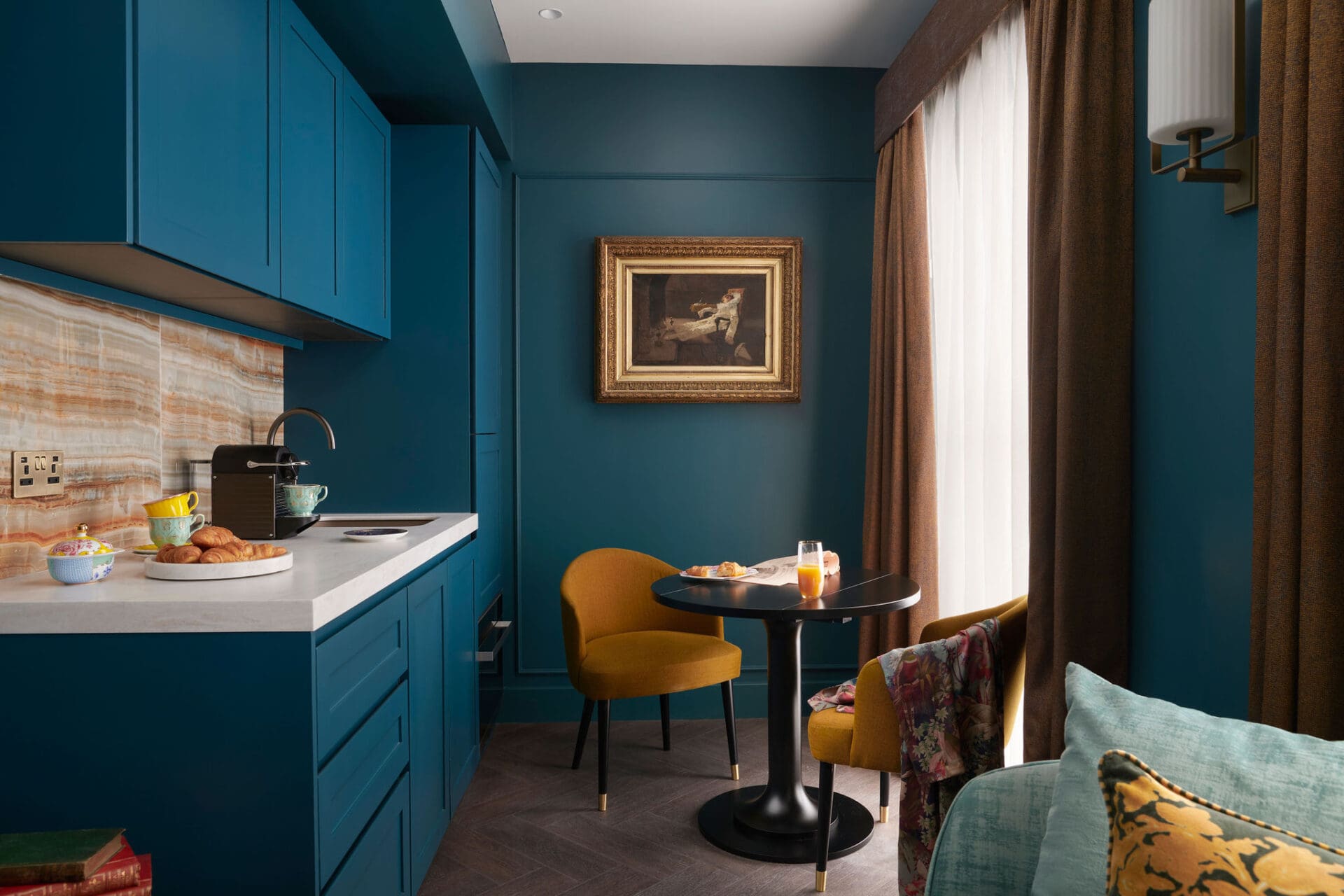 The best hotel openings for summer 2022 | A blue walled kitchen space with mustard-yellow-upholstered furniture at The Other House