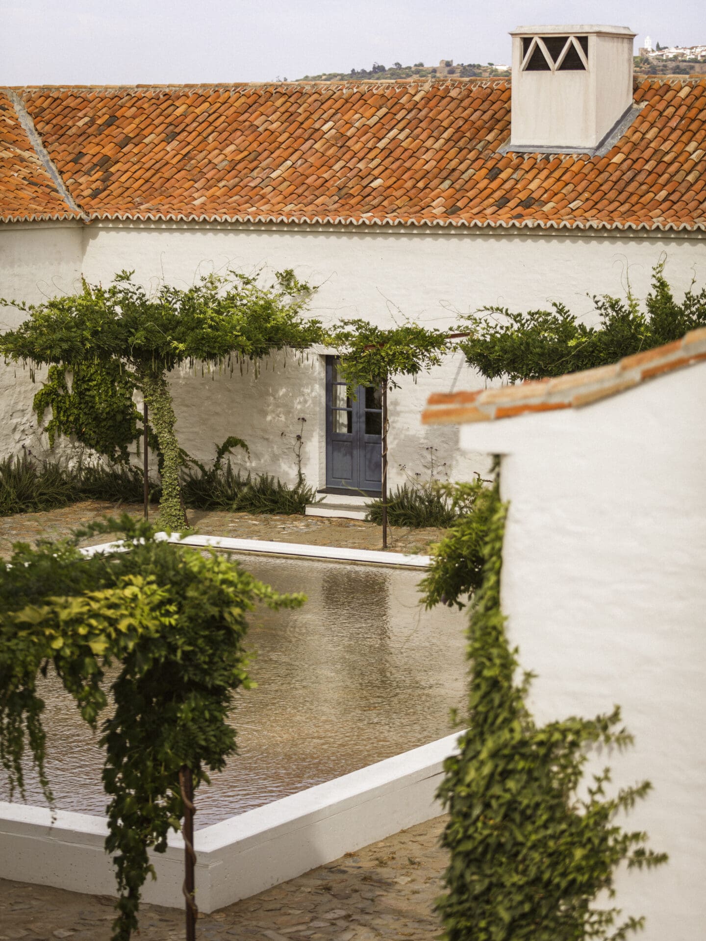 São Lourenço do Barrocal | whitewashed buildings with terracotta-tiled roofs border a shallow square pool, surrounded by vines