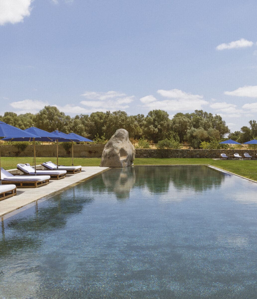 São Lourenço do Barrocal | A neolithic stone juts out of the ground at the corner of a blue swimming pool, surrounded by grass