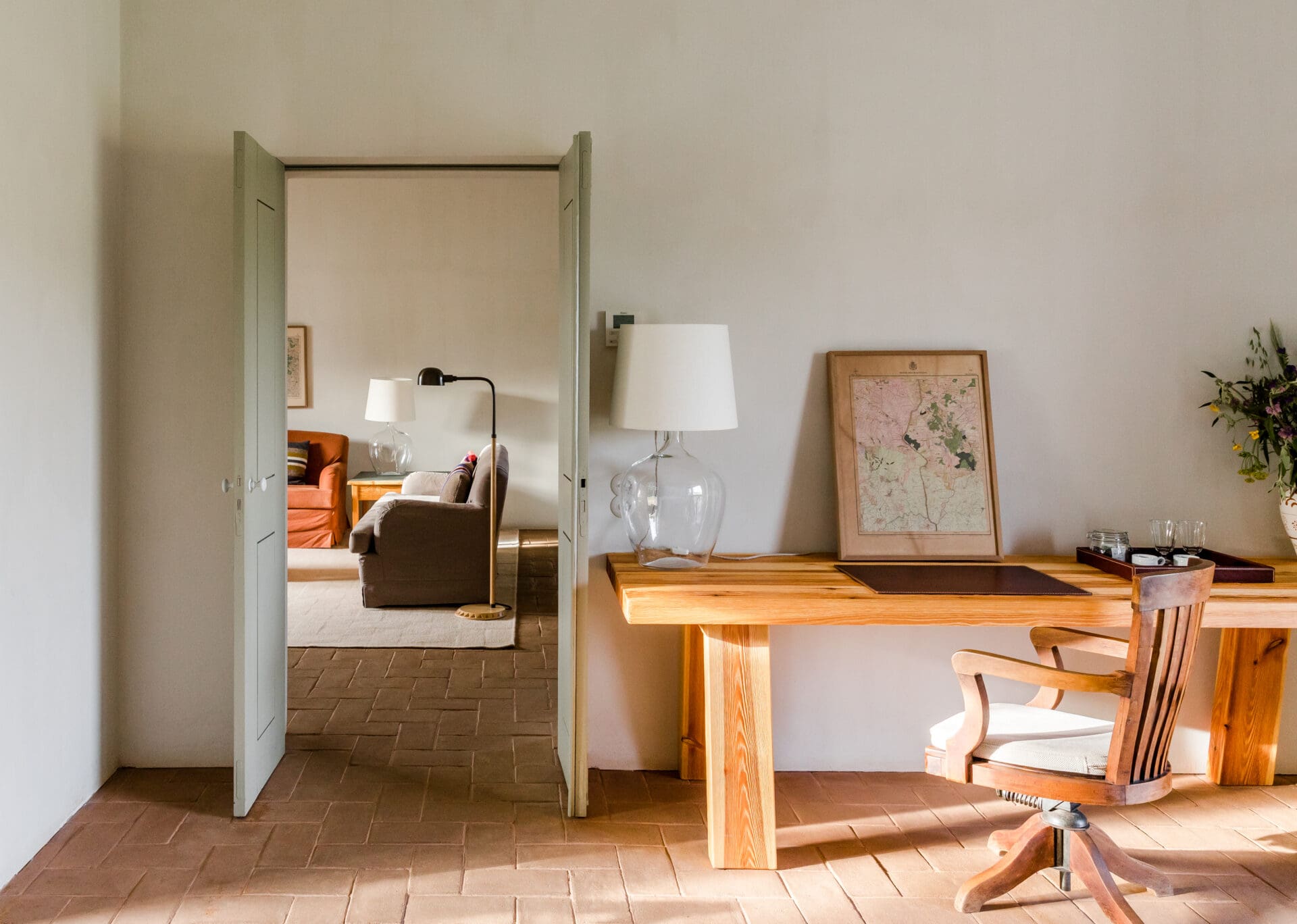 São Lourenço do Barrocal | Inside a suite, a wooden desk and chair sit against a whitewashed wall, with a view into a living room with brown and rust-orange furnishing
