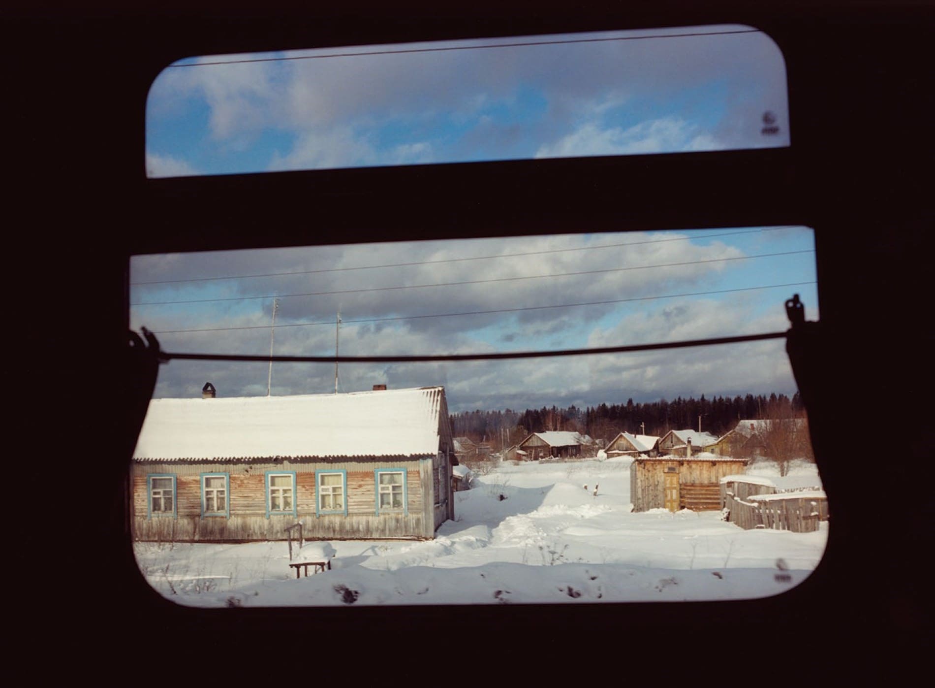 Coco Capitan | A view through a train window of a snow-covered wooden house in Siberia