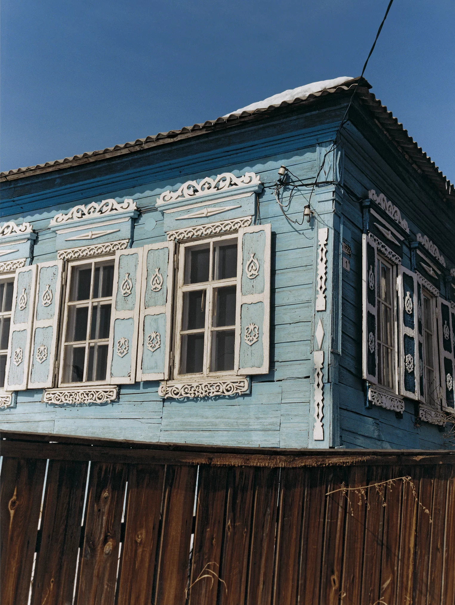Coco Capitan | A blue-boarded wooden house with white shutters on a sunny day in Siberia