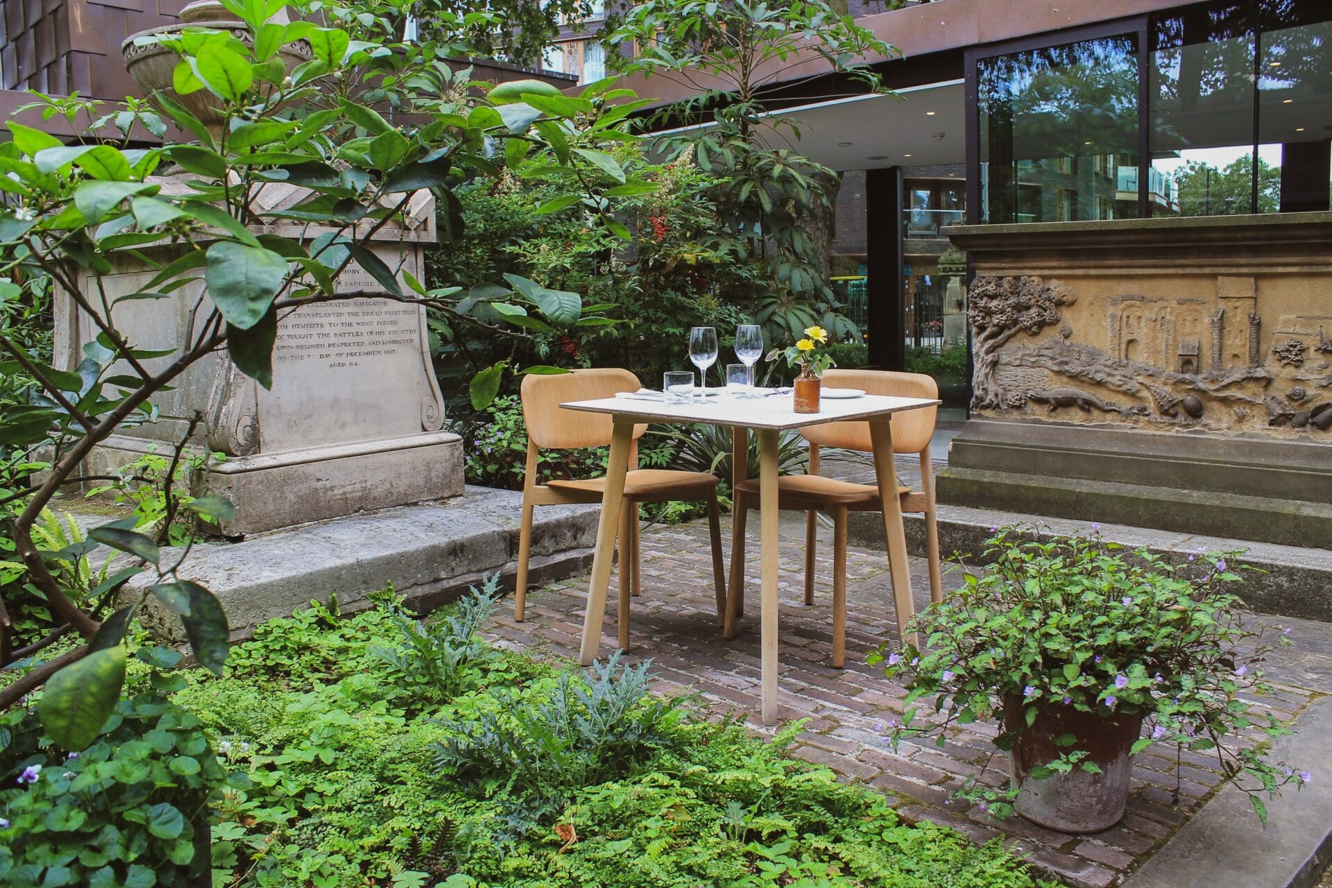 Where to eat al fresco in London | A table in the Garden Museum Café's courtyard, surrounded by greenery and next to a tombsotne