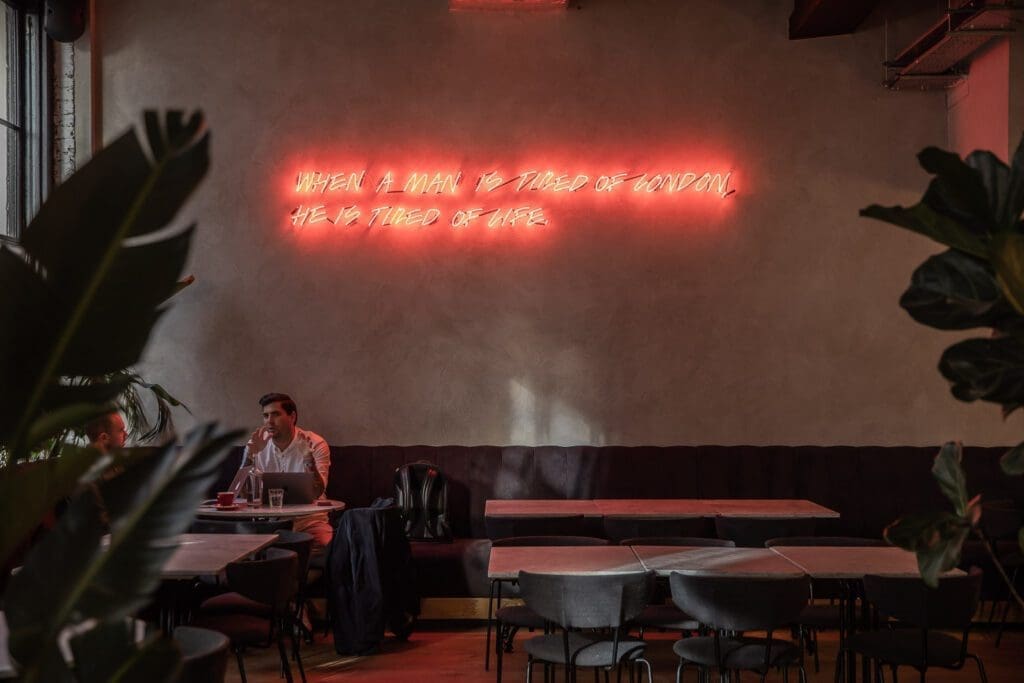 The best European cities for remote working | Inside the London Bridge location of Grind cafe, where a neon red sign can be seen against a mottled, textured wall.