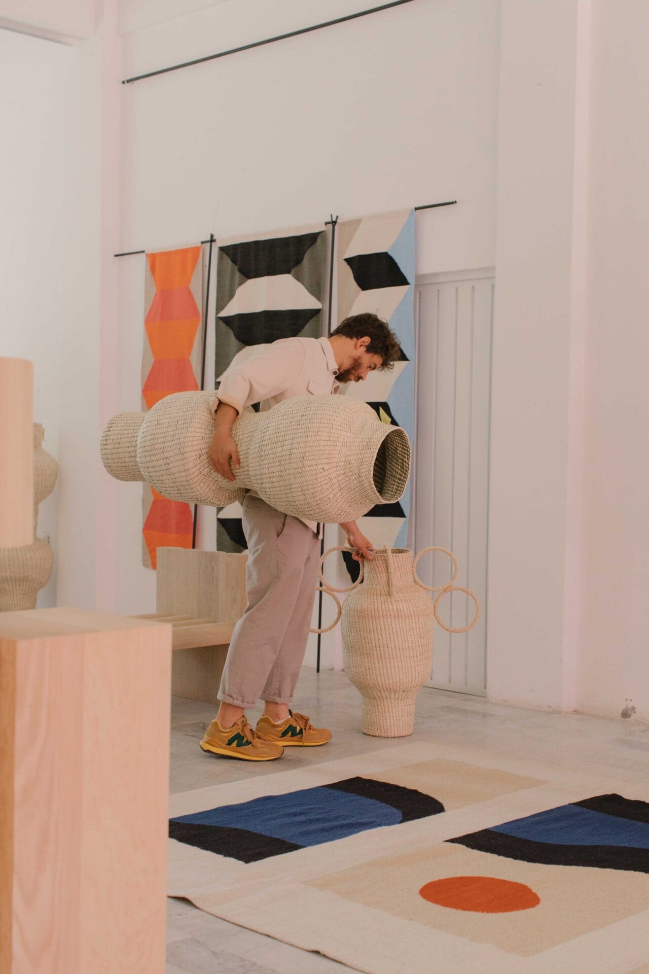 Javier Reyes, rrres studio, Oaxacao | Reyes holds a big woven basket while looking at a woven rug